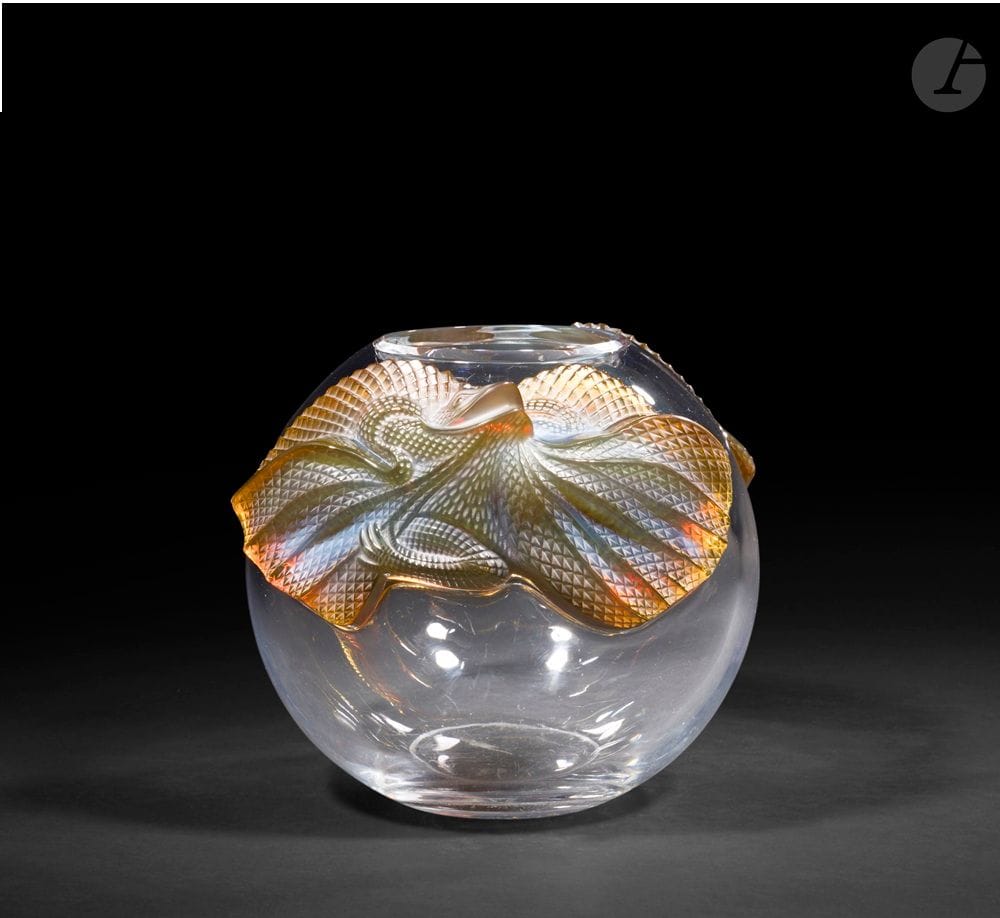 MARIE-CLAUDE LALIQUE (1935-2003) – MAISON LALIQUE
Erimaki, le modèle conçu en [1988]
Vase boule. Épreuve en cristal soufflé-moulé, au décor en applications à chaud de lézards en cristal moulé-pressé teinté ambre dans la masse et satiné. Infimes chocs et égrenures au décor de lézards. Non signé. H. 23 cm – D. 28 cm