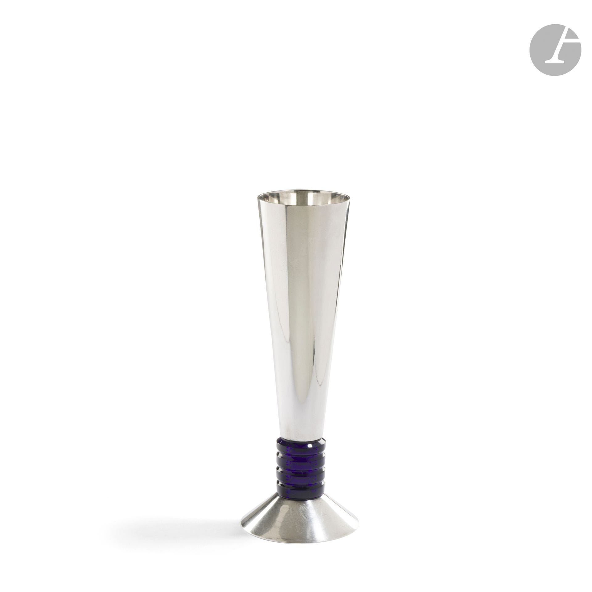 PUIFORCAT FRANCE
Vase cornet à base tronconique. Épreuve en métal argenté. La bague annelée en cristal bleu nuit. Marqué PUIFORCAT France et porte le poinçon de Maître Orfèvre sur le pourtour de la base. H. 20 cm