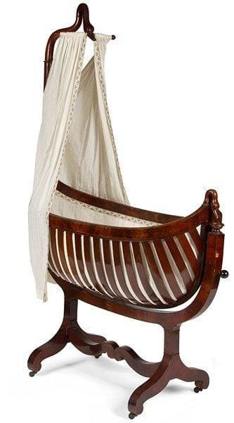 Berceau à nacelle en acajou et placage d'acajou; la nacelle mobile à lattes ajourées se termine par une tête de cygne; le support de voilage en col de cygne, piétement en consoles à entretoise à crosses. Époque Restauration. Quelques éclats au placage et petite restauration d'usage. H.: 186 cm - L.: 124 cm - P.: 63 cm