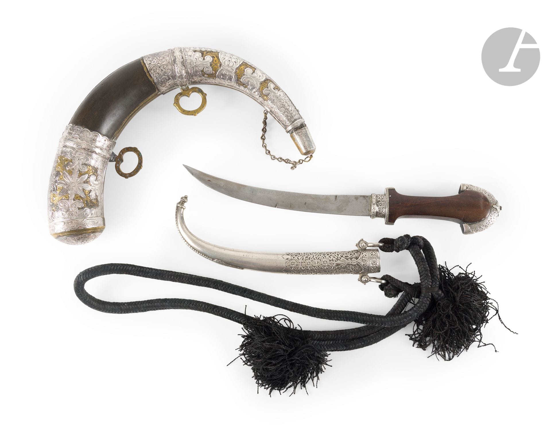 Poignard koumiyya et corne à poudre, Maroc, XXe siècle
Le poignard à manche en bois à garniture en « chapeau de gendarme » en argent gravé, lame courbe à double tranchant et fourreau en argent moulé et ciselé d’un décor floral, flanqué de deux anneaux reliés par un cordon textile noir tressé. Sur la lame, décor ciselé d’un cartouche floral et d’un cavalier dans un médaillon. La poire à poudre en corne à garnitures en métal et laiton ciselées de rinceaux végétaux et rosettes, flanquée de deux anneaux de suspension et fermée d’un bouchon relié à une chaînette. 
L. poignard : 40 cm ; poids brut : 610 g ; L. corne à poudre : 33 cm. 
Poignard : petites rayures, petites traces d’oxydation sur la lame ; corne à poudre : cordon de suspension manquant, une soudure à un anneau, petites rayures et traces d’oxydation.