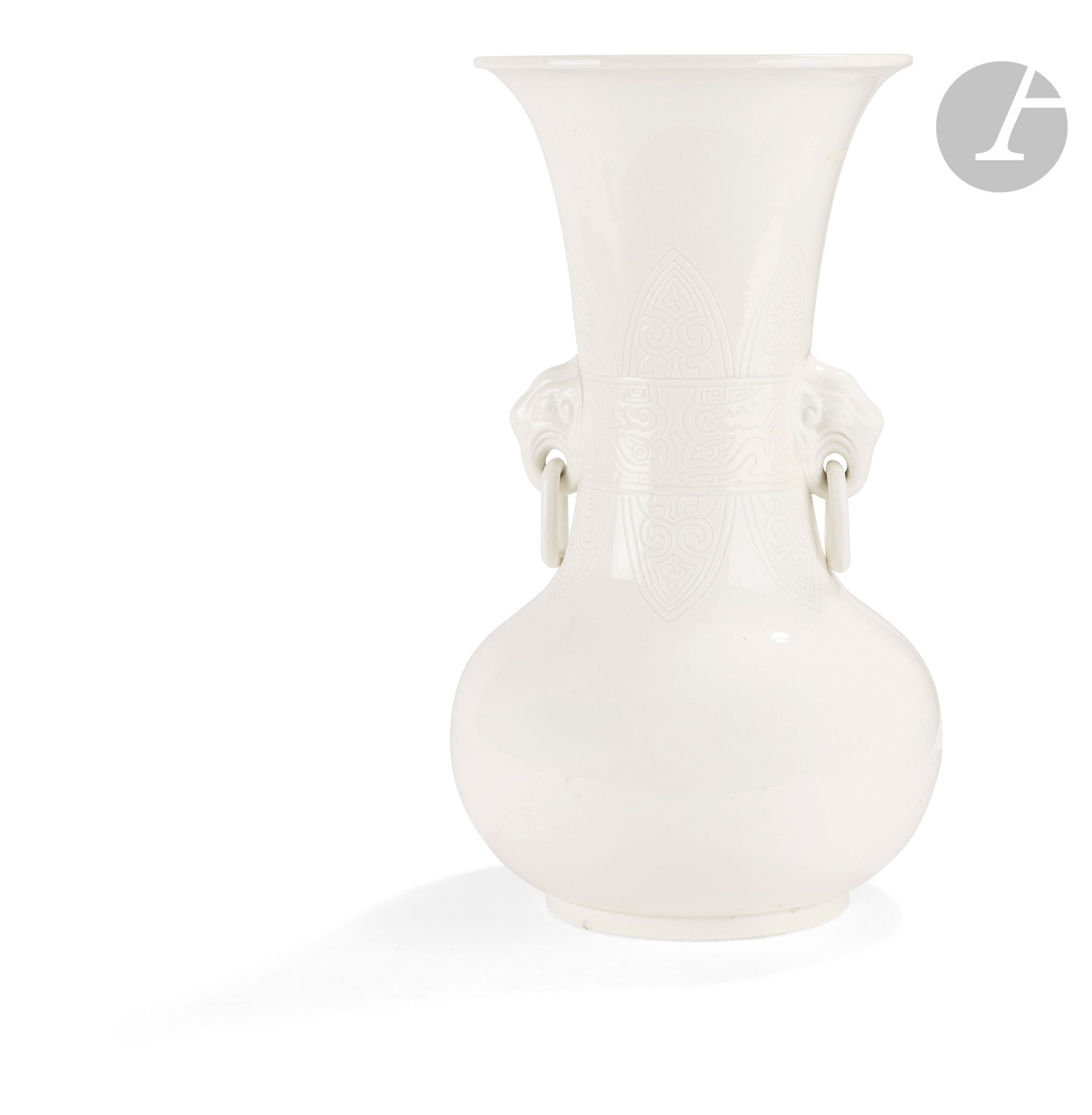Vase en porcelaine blanche, Japon, XXe siècle
La panse globulaire est surmontée d’un col évasé incisé dans sa partie la plus rétrécie dans un bandeau de masques de taotie de style archaïque et de palmettes ornées de têtes de ruyi. Il est flanqué de deux anses moulées en forme d’une tête d’éléphant soutenant un anneau mobile avec sa trompe.
Hauteur : 38 cm
Petite égrenure au talon et fels dans la couverte.