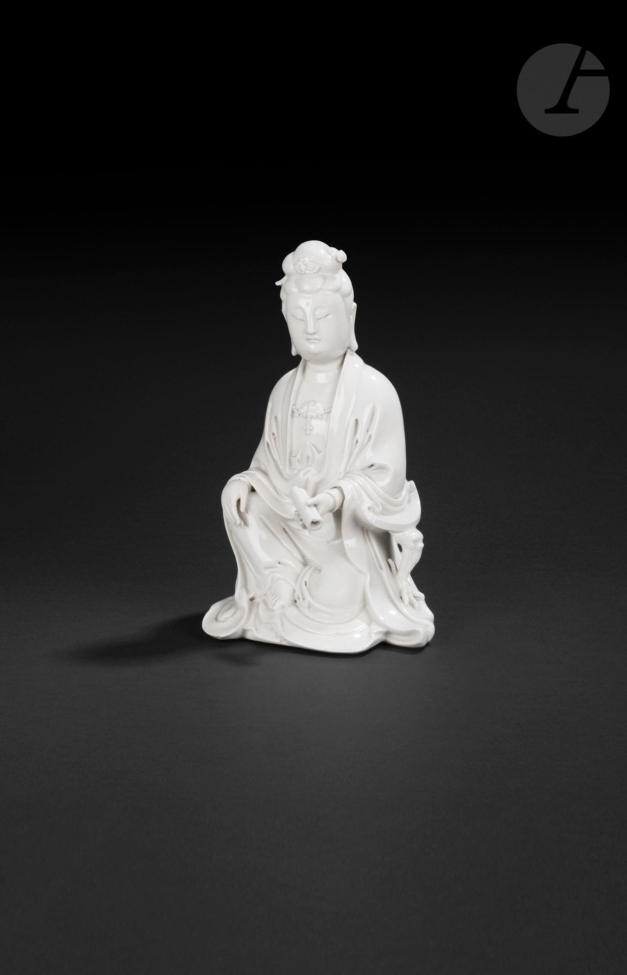 Guanyin en porcelaine blanc de Chine, Chine, Dehua, XIX-XXe siècle
Représentée assise, vêtue de robes superposées tombant en plis autour du corps, le torse paré d’un collier de perles et d’un pendentif en forme de fleur de lotus. Le visage est serein, les yeux baissés et les cheveux sont rassemblés en un chignon coiffé d’épingles. Le front est paré de l’urna et les lobes d’oreille sont allongés. Le bras gauche est posé sur un accoudoir au plateau incurvé reposant sur un pied à tête de dragon terminé par une patte de dragon à quatre griffes accrochée au vêtement. La main gauche tient un rouleau. Le pied droit nu dépasse du bas de la robe. Dans le dos figure une marque carrée moulée, difficilement identifiable. Couverte légèrement craquelée.
Hauteur : 24 cm