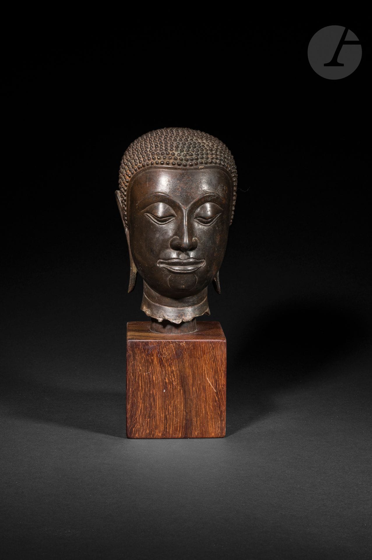 Buddha head in copper alloy with dark brown patina, Thailand, Kingdom of Ayutthaya, probably 17th - 18th century
The face is depicted with half-closed eyes in a meditative expression. The arched eyebrows meet the bridge of the straight, softly-modeled nose. The mouth, with its full lips, sketches a light, serene smile. The earlobes are elongated, symbolizing the renunciation of princely finery. The hair is in tight curls, covering the skull cap. No protruding ushnisha.
Mounted on a modern wooden base.
Height: 15.5 cm

Core thermoluminescence test QED1644/FB-0502 of November 21, 2016.