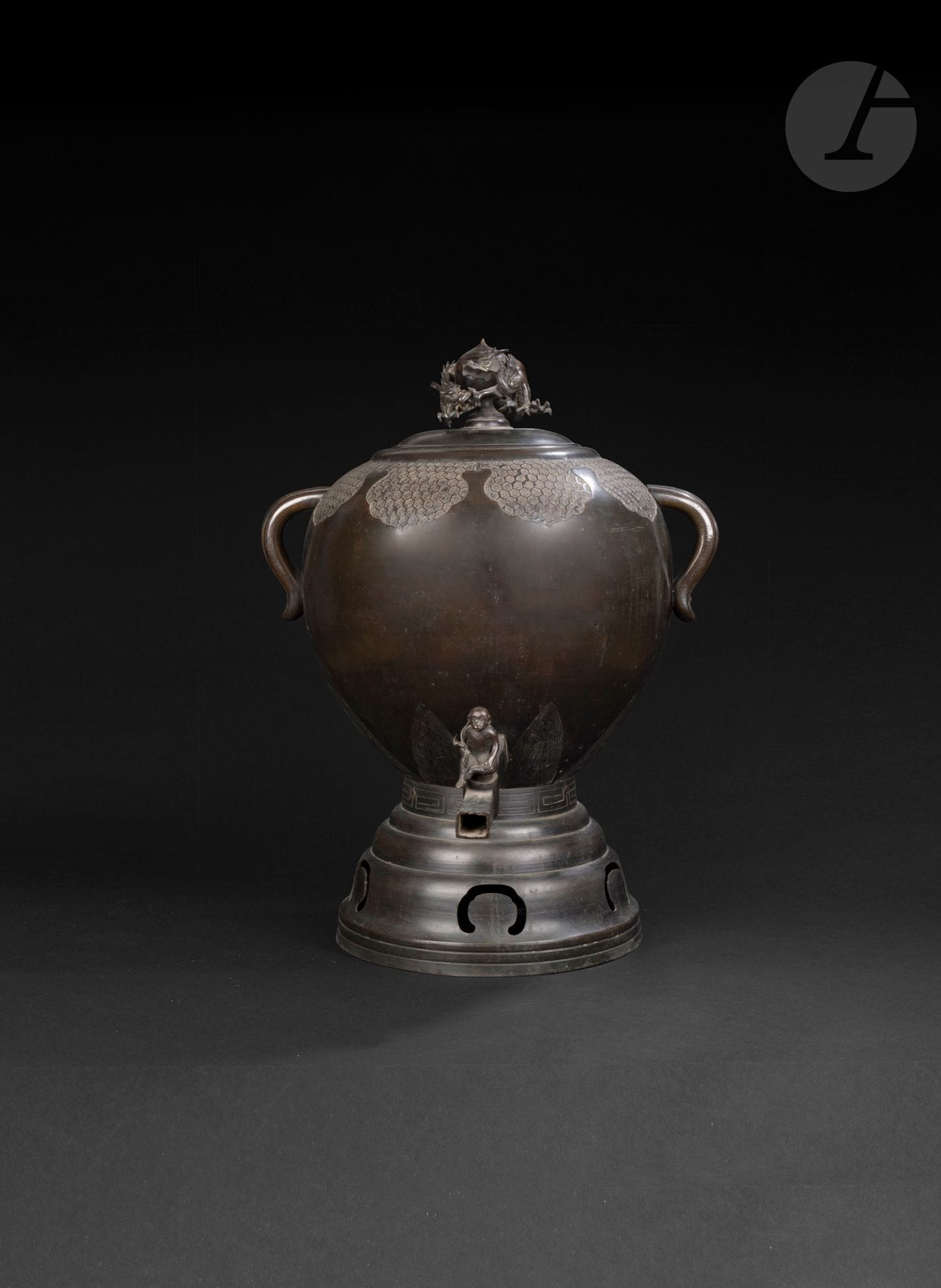 Grande fontaine à eau en bronze, Japon, époque Meiji (1868-1912)
La panse globulaire rappelant le tama est flanquée de deux anses incurvées. La prise du couvercle figure un dragon en relief s’enroulant autour du joyau sacré. Autour de l’ouverture, tourne une large frise à motif kikkô dit écaille de tortue. Au bas de la fontaine, le bec verseur est muni d’un robinet sculpté en ronde bosse en forme de singe. L’ensemble est monté sur un pied circulaire étagé à motif de grecques sur la bande supérieure. 
Hauteur : 71 cm
Les dragons détachés, un cassé.