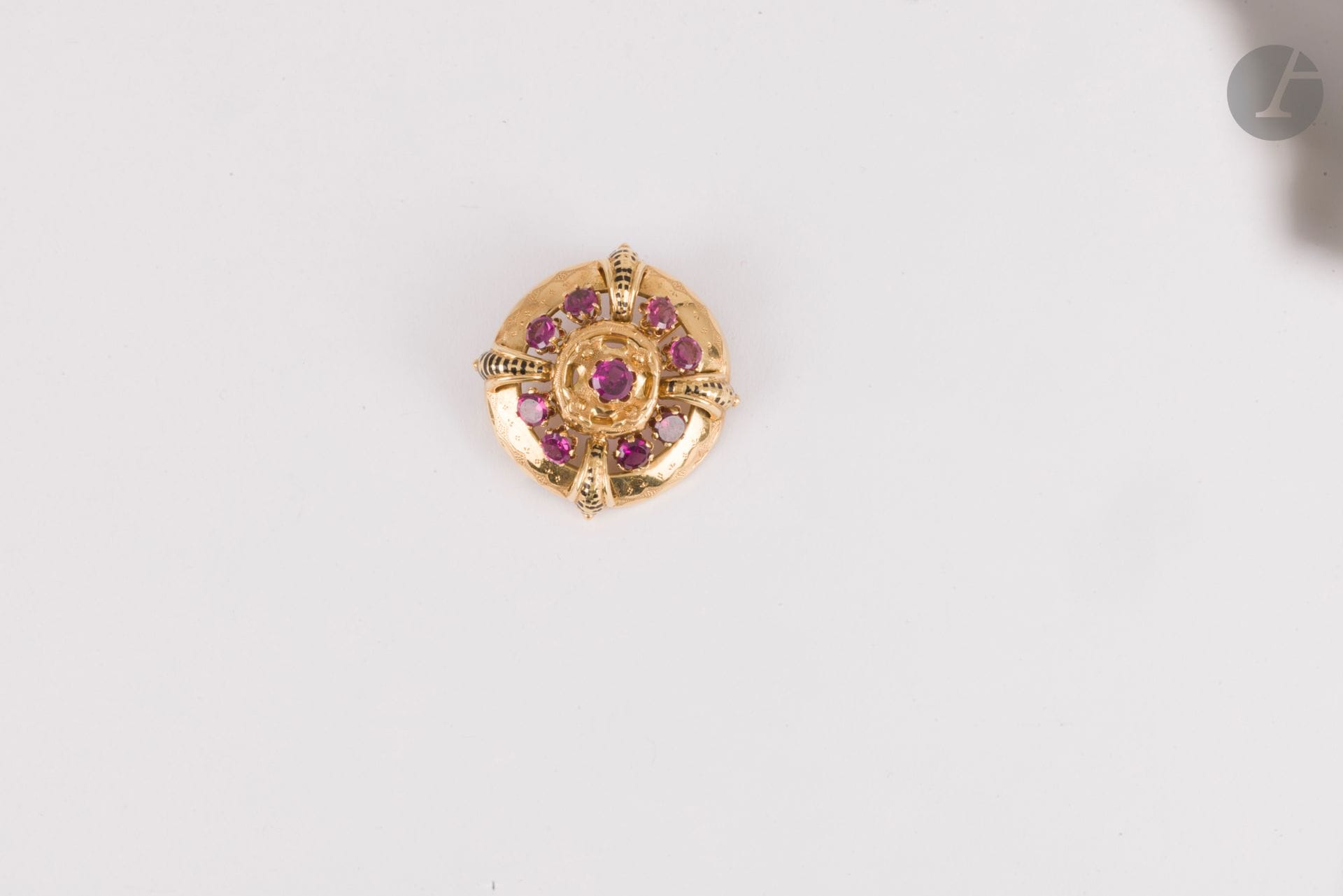 Broche ronde en or 18K (750) repercé, ornée de pierres violettes, soulignée d'émail noir. Travail de la fin du XIXe siècle. Diamètre : 3 cm environ. Poids brut : 7,3 g (enfoncement, manques à l'émail, une pierre à ressertir)
