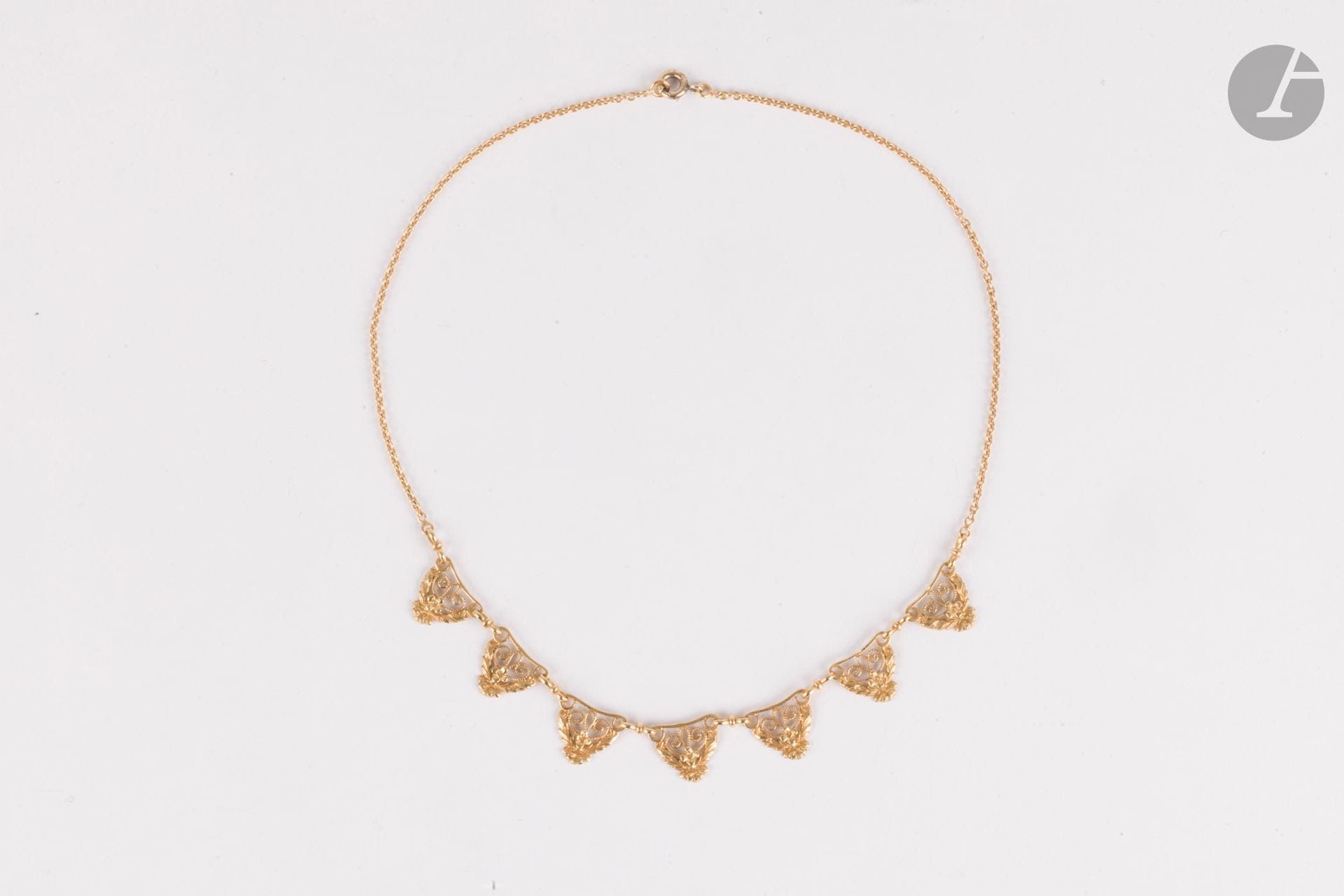 Collier en or 18K (750), centré de 7 motifs filigranés agrémentés de fleurs stylisées. Longueur : 38 cm environ. Poids : 9,4 g