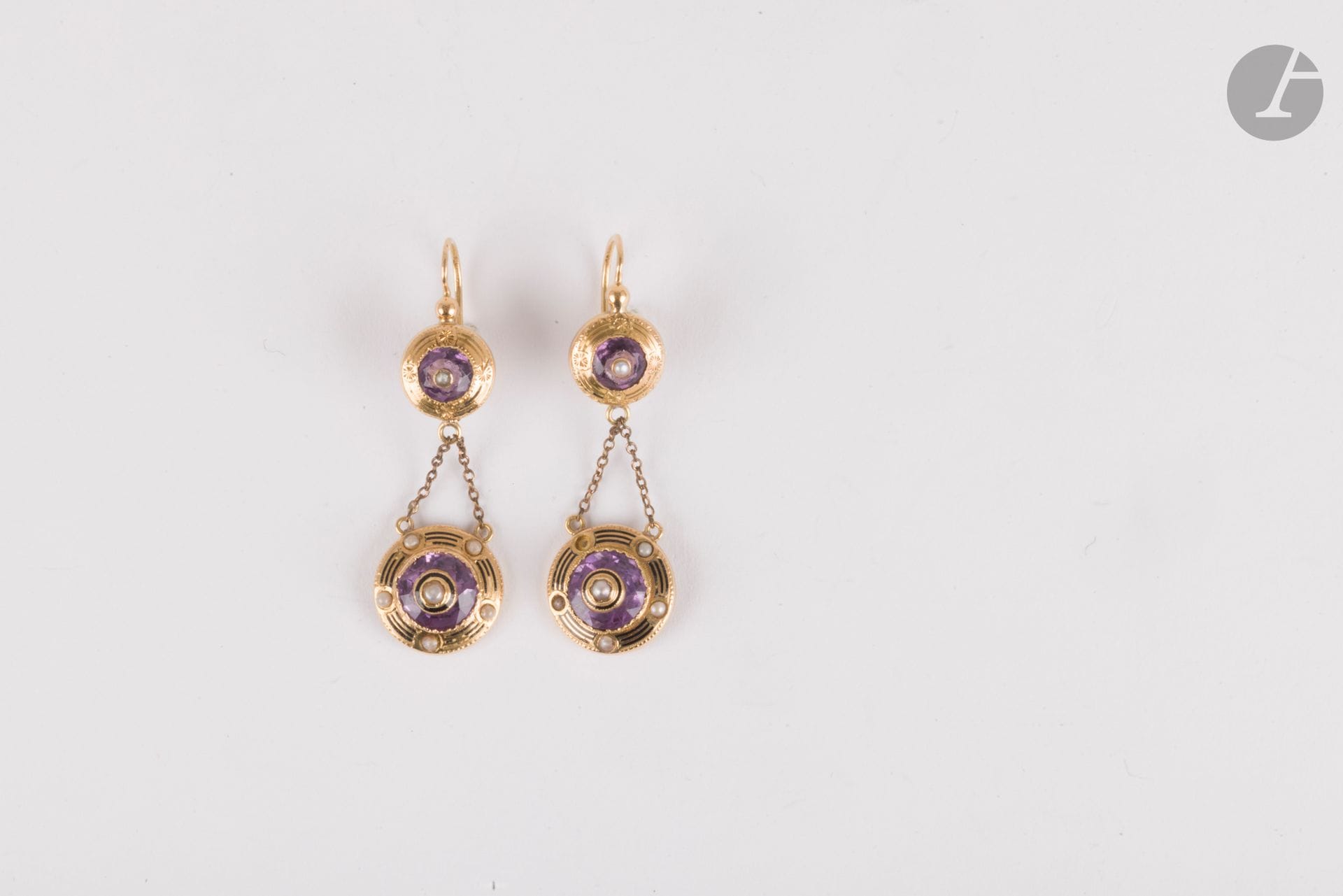 Paire de pendants d'oreilles en or 18K (750), chacun orné d'une améthyste piquée d'une demi-perle, retenant par deux chaînettes, une améthyste entourée de demi-perles naturelles ou fantaisie, souligné de filets émaillés. Travail français de la fin du XIXe siècle. Hauteur : 4,5 cm environ. Poids brut : 5,2 g (manques, perles changées, colle)