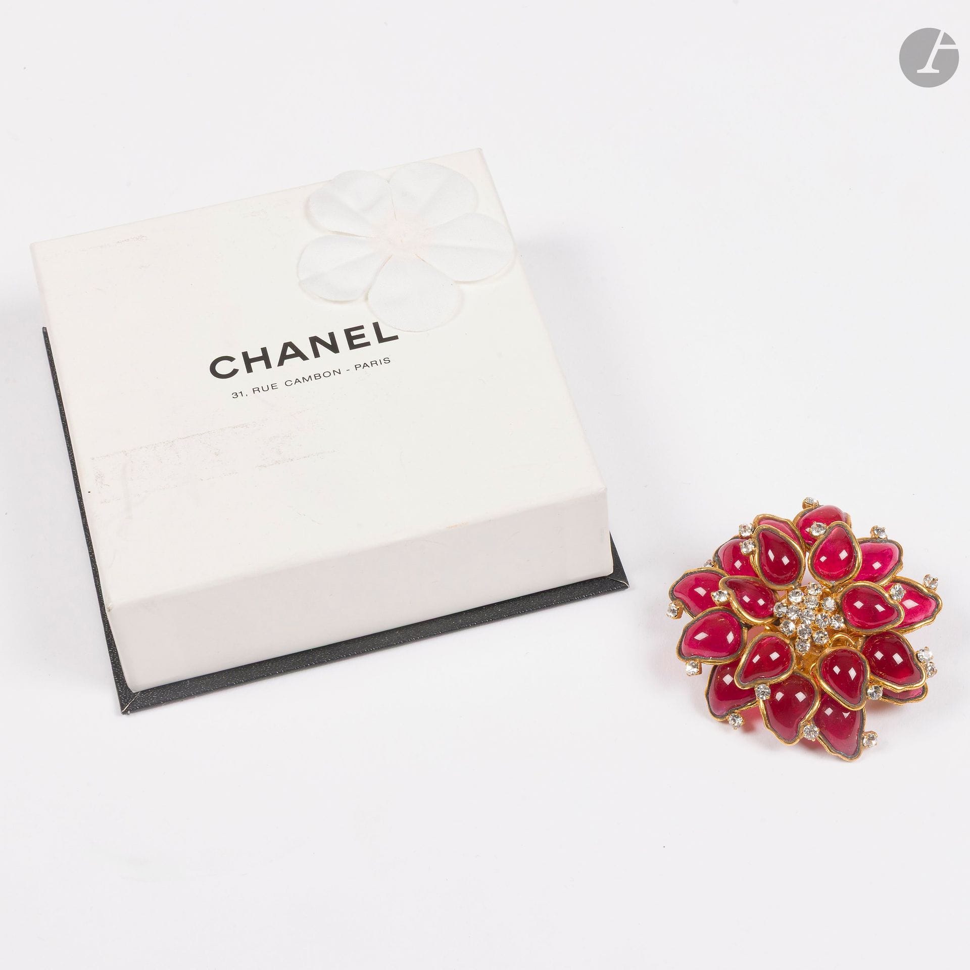 CHANEL
Broche fleur en métal doré, pétales en pâte de verre rouge, cœur et décor de strass. Signée. H : 5,5 cm. Dans sa boîte accidentée