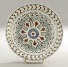Plat tabak à la rosace festonnée, Turquie ottomane, Iznik, fin du XVIe siècle Céramique siliceuse à base annulaire à décor peint en polychromie sur fond blanc sous glaçure transparente. Une large rosace se développe sur un fond vermiculé dans un médaillon flammé. Au rebord, frise d?églantines superposées sur fond bleu. Diam.: 30 cm et H.: 5,8 cm Voir un plat au décor similaire dans le catalogue, Sotheby?s Londres, 24 avril 2012, lot 151. An Iznik polychrome pottery dish, decorated with a central scalloped roundel, Ottoman Turkey, end of 16th century.(*)