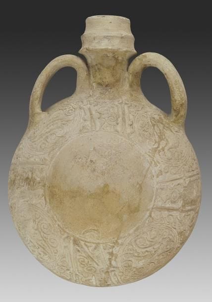 Gourde aux paons, Syrie, XIIe-XIIIe siècle Terre cuite à panse circulaire bombée, à deux anses et col annelé. Décor moulé sur le pourtour de la panse d?une frise épigraphique alternant coufique et naskhî foliés interrompue de rondeaux meublés de paons, sur fond de rinceaux sur une face, et d?une frise de godrons sur l?autre. L.: 23 cm An unglazed flask with moulded decoration of peacocks, Syria, 12th-13th century