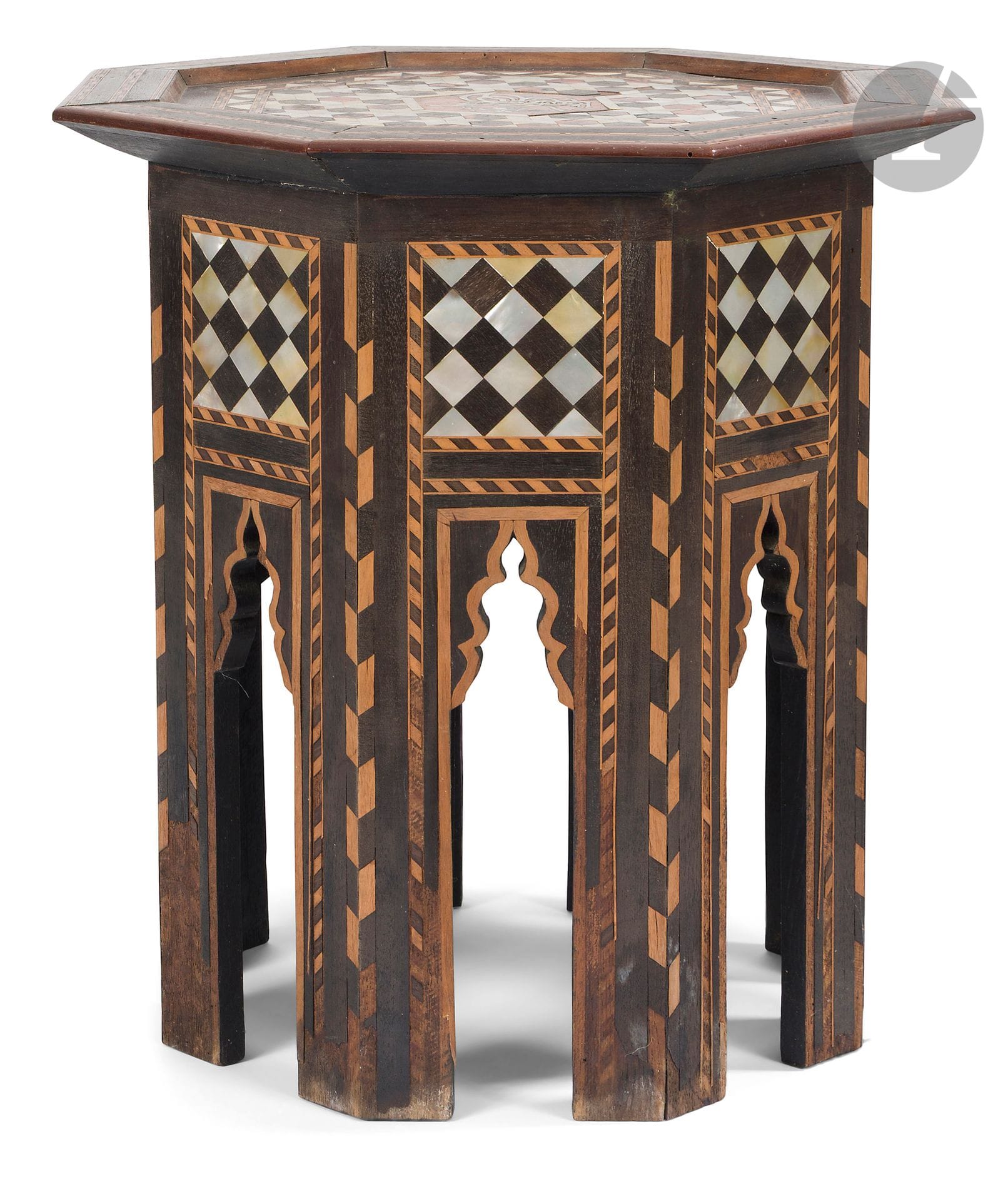 Salon en bois, Syrie, début XXe siècle
Salon en bois gravé, champlevé et incrusté de nacre et d’os, composé d’une banquette, d’une paire de chaises et d’un guéridon. La banquette à assise rectangulaire reposant sur quatre pieds, les accoudoirs courbés vers l’extérieur et ajourés de trois arcatures en accolade. Décor de rinceaux végétaux et de frises tressées ; la paire de chaises pliantes ornée de rinceaux végétaux ponctués de disques ou étoiles incrustés de nacre. Le sommet du dossier en forme de mandorle polylobée logeant un motif de croissant de lune embrassant une étoile incrustée de nacre ; le guéridon à plateau octogonal reposant sur une base à pans coupés, chacun découpé d’une niche flanquée de deux pieds. Fin décor marqueté de modules géométriques, d’un large registre octogonal logeant une pseudo-tughra et d’un motif floral au centre du plateau.
Banquette : H. 70 cm, L. 85,5 cm, l. 45,5 cm
Chaises : H. 102 cm, assise 32 x 30 cm
Guéridon : H. 45 cm, d. max : 45 cm
Usure, rayures, petits manques et accidents, soulèvements de marqueterie et trous de xylophages sur le guéridon.