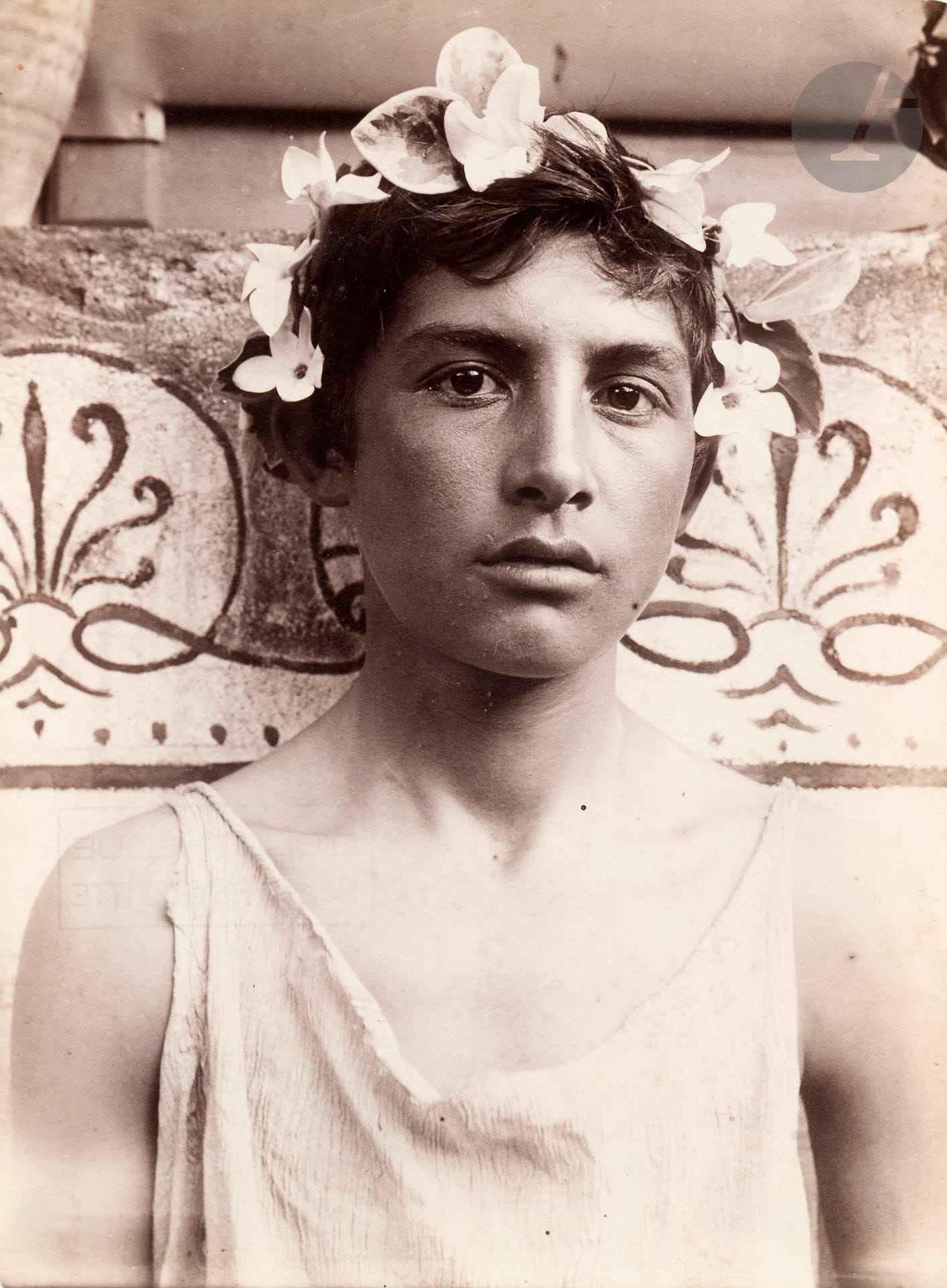 Wilhelm von Gloeden (1856-1931)
Jeune sicilien [Giacomo Lanfranchi] à la couronne de passiflores. Taormina, Sicile, c. 1895.
Épreuve sur papier albuminé. Tampons « W. v. Gloeden - Kunstverlag - Deponirt 23 Juil. 1903 - Taormina Sicilia », « W. von Gloeden - Taormina (Sicilia) » et « Bibliothèque - Roger Peyrefitte » avec numéro de négatif « 1748b » au crayon bleu au verso.
22,5 x 17 cm

Provenance : 
Ancienne collection Roger Peyrefitte. 

Bibliographie : 
Raffaella Perna, Wilhelm von Gloeden. Travestimenti, ritratti, tableaux vivants, Milan, Postmedia Books, 2013, fig. n°17.