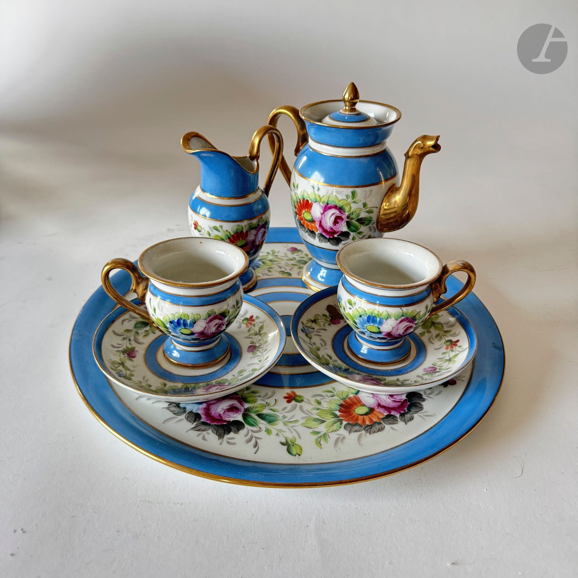 Service tête-à-tête en porcelaine bleu et blanc et rehauts doré à décor floral comprenant :
- Une cafetière, 
- Un pot à lait, 
- Deux tasses, 
- Deux soucoupes, 
- Un plateau.
Porte une marque sous la base : "N couronné". 
Diamètre du plateau : 33 cm