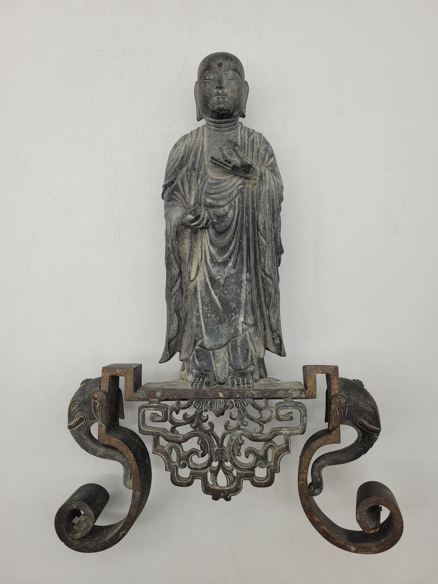 Figure de Jizo Bosatsu debout en alliage cuivreux, Japon, XIXe siècle 
Debout, tête rasée, les yeux fermés, sous sa forme monastique, tenant dans sa main gauche un joyau bouddhique. Sur une monture ajourée européenne postérieure à deux volutes ornées de têtes d’éléphant sur les côtés. Inscription donnant son nom au dos.
H. Jizo : 27 cm ; h. totale : 40 cm