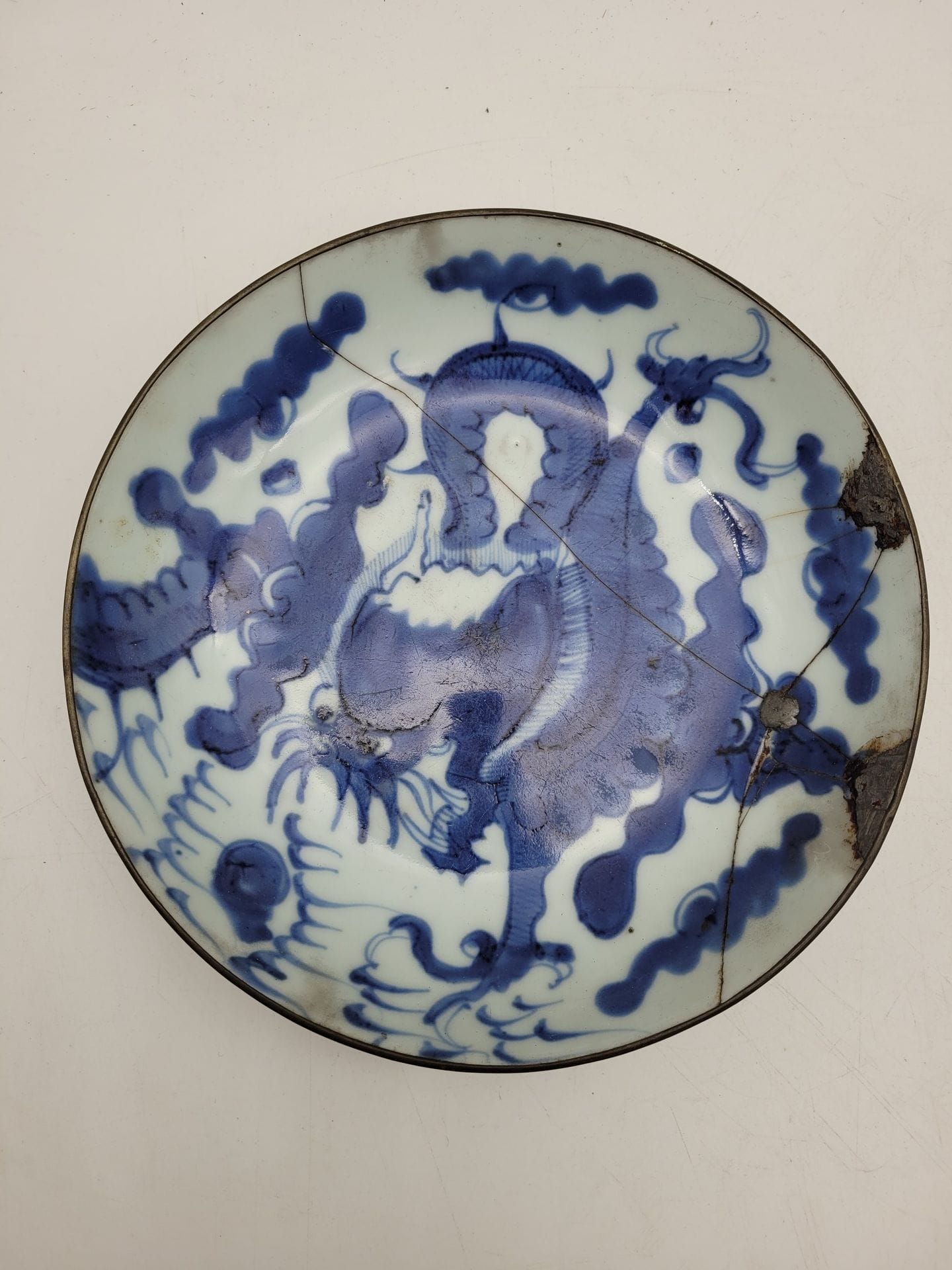 Plat en porcelaine à décor bleu-blanc, Chine pour Vietnam, XIXe siècle
Dit bleu de Hue, à décor de dragon pourchassant la perle.
Diamètre : 20,4 cm
Marque sous la base.
Bord et pied cerclés de métal. Cassée-collée et restaurations à l'étain.