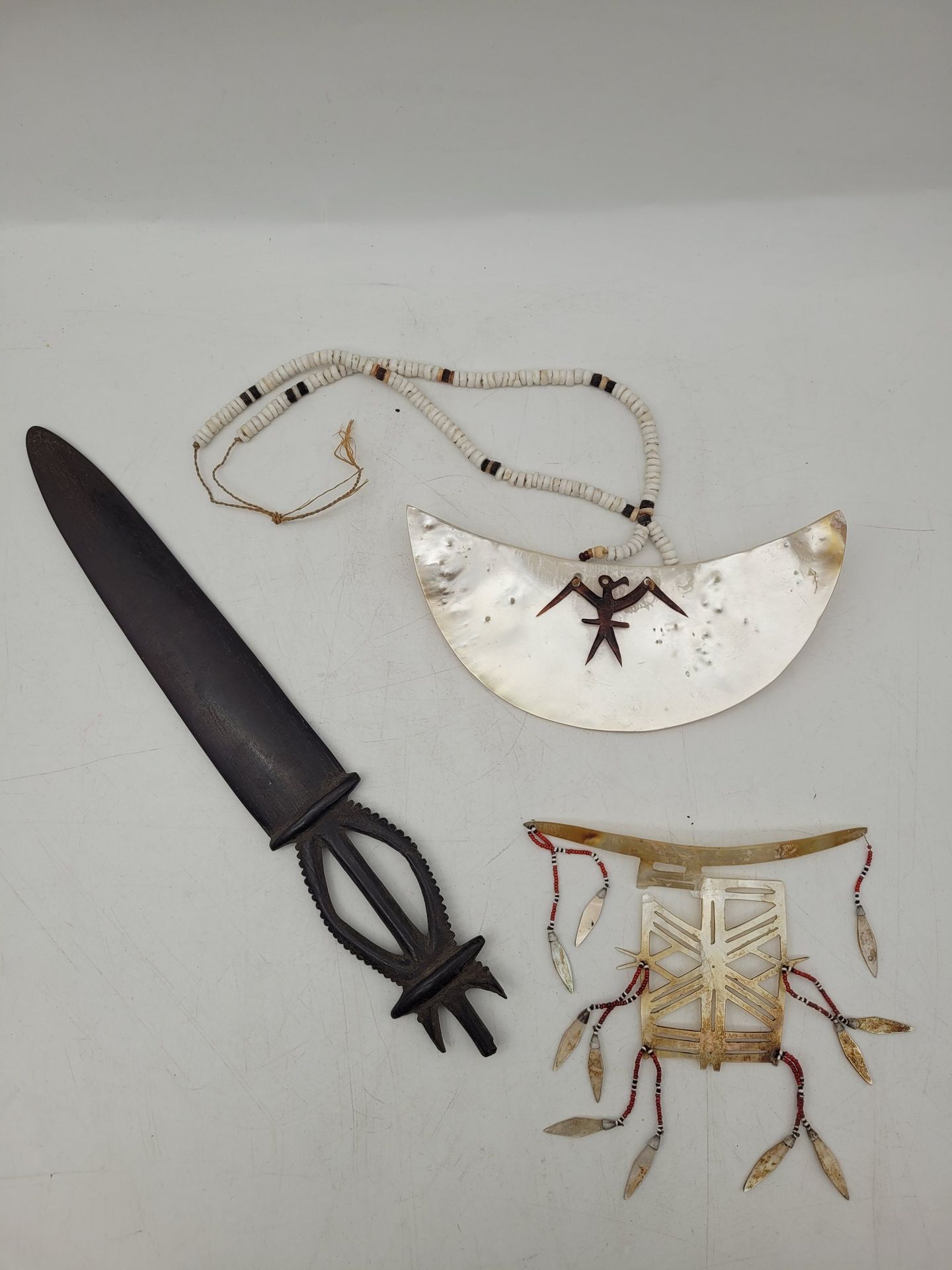 Ornement de nez et collier pectoral, Iles Salomon
Hauteur ornement : 8 cm ; largeur pectoral : 16 cm
Cassure pour l’ornement. 
On joint :
Couteau à igname en bois, Îles Banks (Vanuatu). Long. : 30,4 cm ; 
petit personnage assis en terre cuite, de style syro-hittite. H. : 7 cm et élément en os à décor géométrique. L : 10 cm