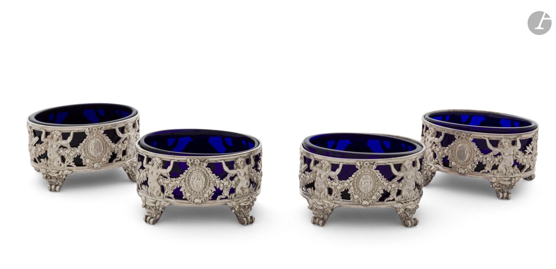PARIS 1779 - 1780
Set of four oval salt cellars in chased cast silver, complete with blue glass. Four scrolled feet seem to serve as pedestals for the body, decorated with two mermaids on either side framing an enrubanné medallion engraved with a coat of arms. 
Master silversmith: François-Alexis CARRON, received in 1777
Net weight: 398 g