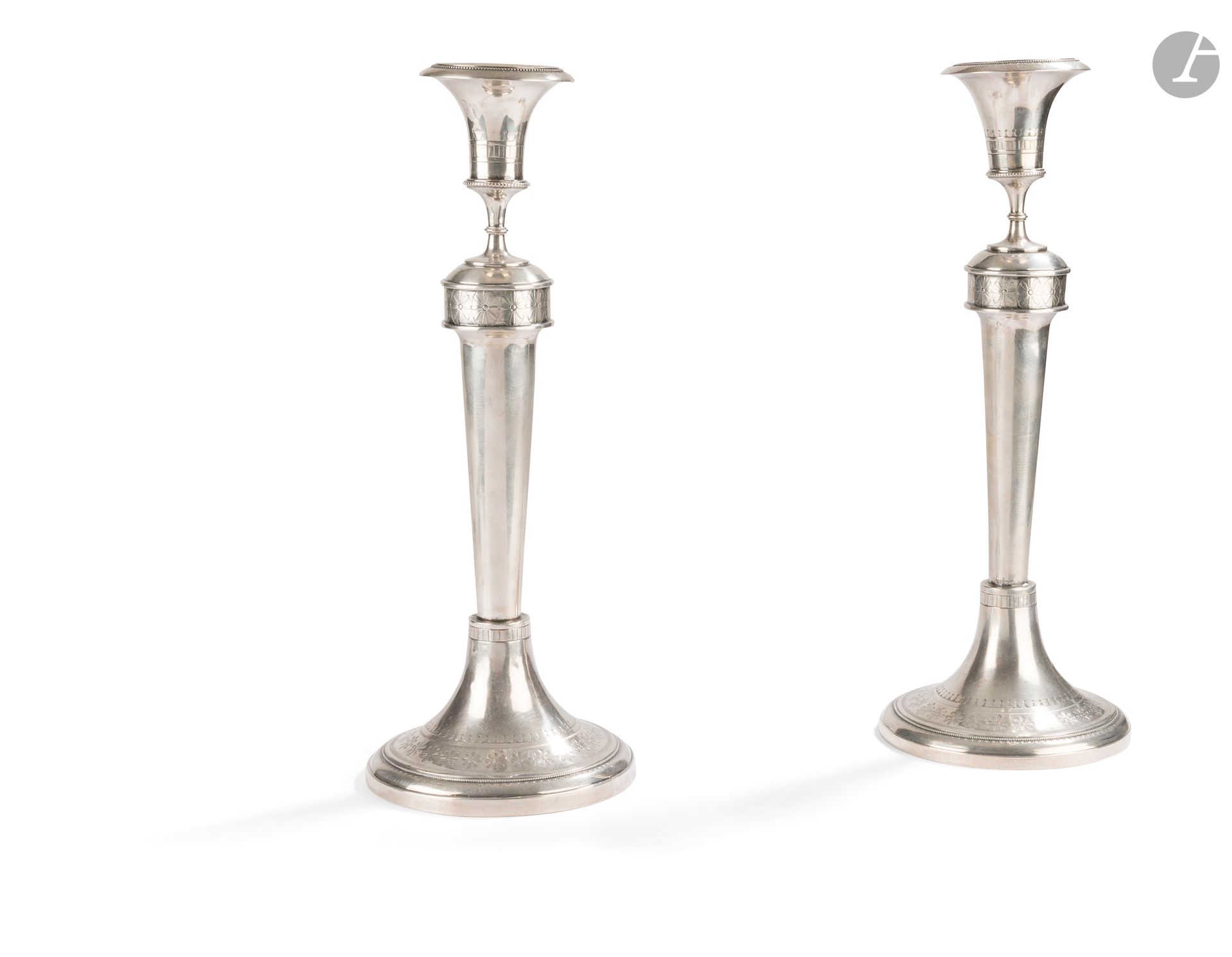 GAND - GENT 1798 - 1809
Paire de bougeoirs en argent 800°/°° reposant sur une base circulaire ciselée successivement d'un rang de perles et de fleurs à huit pétales en rappel sur le haut du fût de forme tronconique, les perles en rappel sur le binet et la bobèche intégrée.
Poids : 815 g - hauteur : 31 cm - diamètre de la base : 11,8 cm
Poinçons français : de second titre et du bureau de garantie n°27 (Escaut)