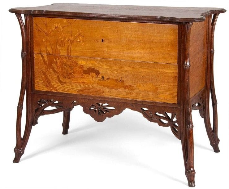 Émile GALLÉ (1846-1904)
La Berce des près, circa 1902/03, unique exemplaire connu à ce jour
Exceptionnelle commode, dite Sauteuse, en placage de frêne et en hêtre sculpté et teinté.
Le corps suspendu reçoit les deux tiroirs au décor en façade, de Berces des près bordant un marais présentant des nénuphars et animé d’une grenouille, réalisé en marqueterie de bois précieux et indigènes.
La ceinture ajourée et sculptée reprend le thème décoratif des ombellifères.
Les quatre jambages d’angle sont traités et sculptés dans le goût arborescent.
Le dessus est constitué d’un plateau chantourné en débordement.
Le dos panneauté est exécuté en noyer.
État et restaurations d’usage, partie centrale de la ceinture ajourée refaite.
Signée GALLÉ en lettres japonisantes verticales dans le décor en marqueterie. 
84 x 107 x 63 cm
Important :
De la série de mobilier La Berce des près par Émile Gallé, seul ce modèle de commode avait échappé à toute iconographie, ancienne ou moderne. N’étaient connus, jusqu’aujourd’hui, que les dessins préparatoires du meuble, de certains de ses détails ainsi que le calque d’exécution du décor en marqueterie, l’ensemble de ces documents étant conservé au Musée d’Orsay.
Bibliographie :
« Gallé Furniture » par Alastair Duncan et Georges de Bartha. Éditions Antique Collectors’ Club, Woodbridge, Suffolk, U. K., 2012. Le dessin préparatoire et le calque d’exécution du décor en marqueterie de ce modèle de commode, deux documents conservés au Musée d’Orsay, sont reproduits page 330