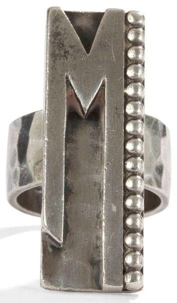 Jean DESPRÉS (1889-1980)
Très rare bague moderniste en argent.
Le large anneau martelé reçoit une longue plateforme rectangulaire excentrée au décor, en applications, d’un M et d’une rangée de sphères sur fond martelé.
Porte les poinçons de Maître Orfèvre et de titre.
Poids : 19 g
