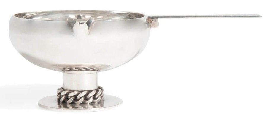 Jean DESPRÉS (1889-1980)
Élégante saucière en métal argenté.
La coupe repose sur un pied cylindrique accueilli par une base circulaire martelée et ornée d’une gourmette à maillons plats.
La prise, ornée d’un cylindre, est à surface martelée.
Signée J. DESPRÉS à la pointe et porte le poinçon de Maître Orfèvre au revers de la prise.
7 x 20,5 x 13 cm
On y joint la carte de visite de l’artiste