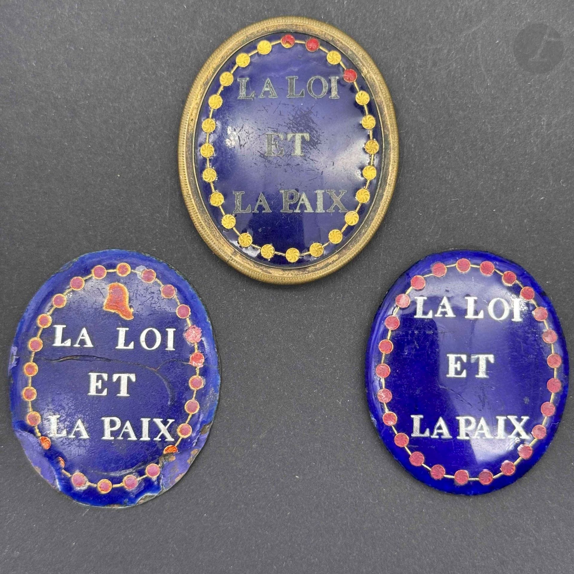 FRANCE
Médaillon émaillé de juge de paix. Cerclage en laiton, centre émaillé bleu avec inscription à l’argent: «la loi et la paix » à bordure perlée émaillée rouge (manques). Revers en tôle (manques deux anneaux d’attache). 
45 x 37 mm 
On y joint deux médaillons du même modèle à légende argentée et bordure perlée, un au bonnet phrygien (accidents et éclats). 
40 x 35 env. 
A.B.E. Époque révolutionnaire.
