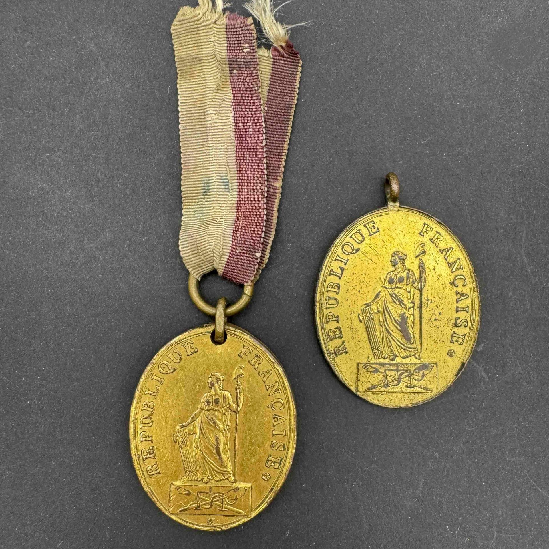 FRANCE
Deux insignes de fonction du tribunal criminel en laiton doré signé Maurisset. 
Un à anneau fixe et un à suspente artisanale à double anneaux et fin ruban tricolore. 
41 x 33 mm 
A.B.E. Époque révolutionnaire.