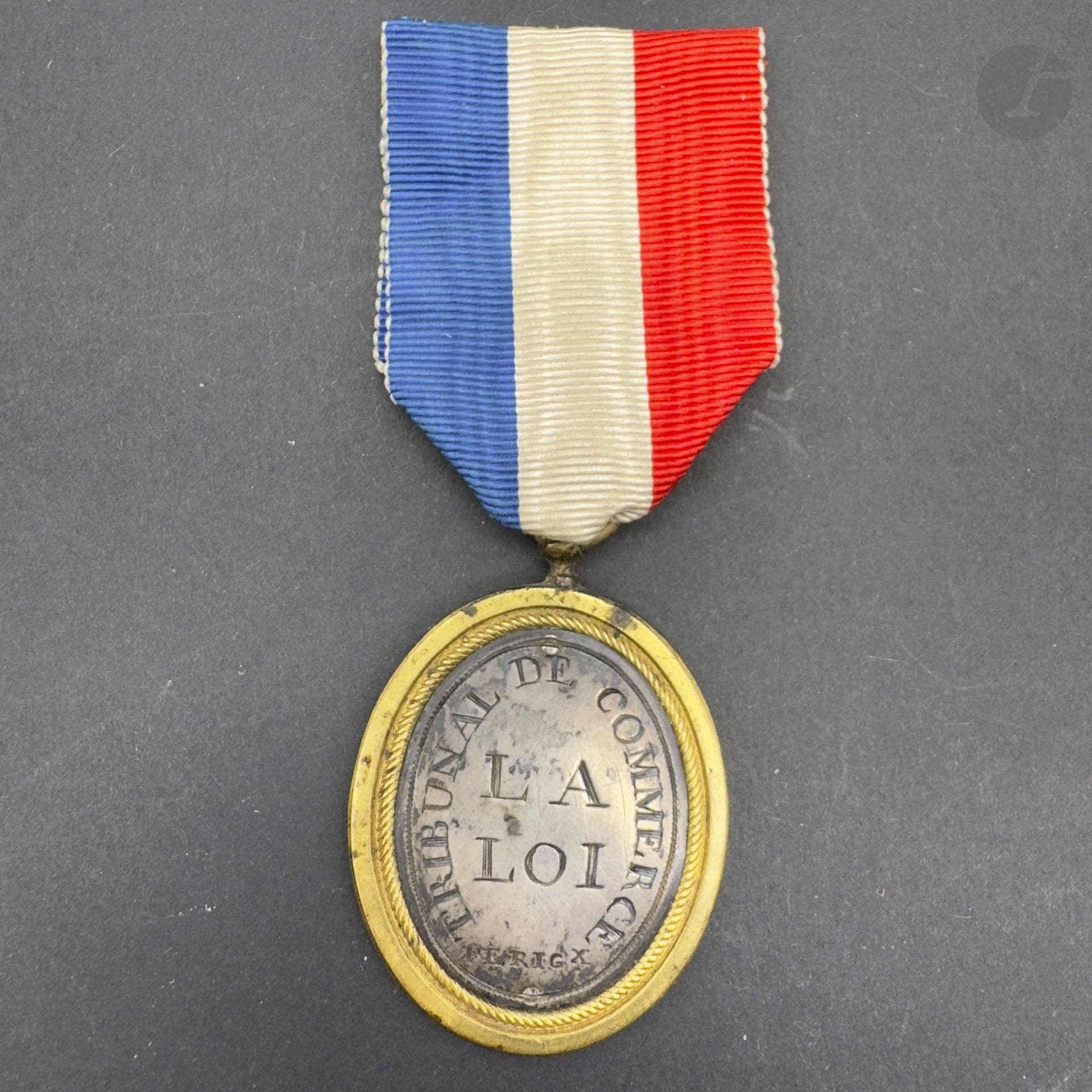 FRANCE 
Insigne de juge de tribunal de commerce de Périgueux. Cerclage en bronze argenté avec jeton argenté, gravé sur une face: «liberté, égalité, justice » à la balance et au bonnet phrygien, signé « M » en bas. Au revers tribunal de commerce «perigx – la loi ». Ruban tricolore postérieur.
51 x 36 mm 
A.B.E. Reproduction du centenaire.
