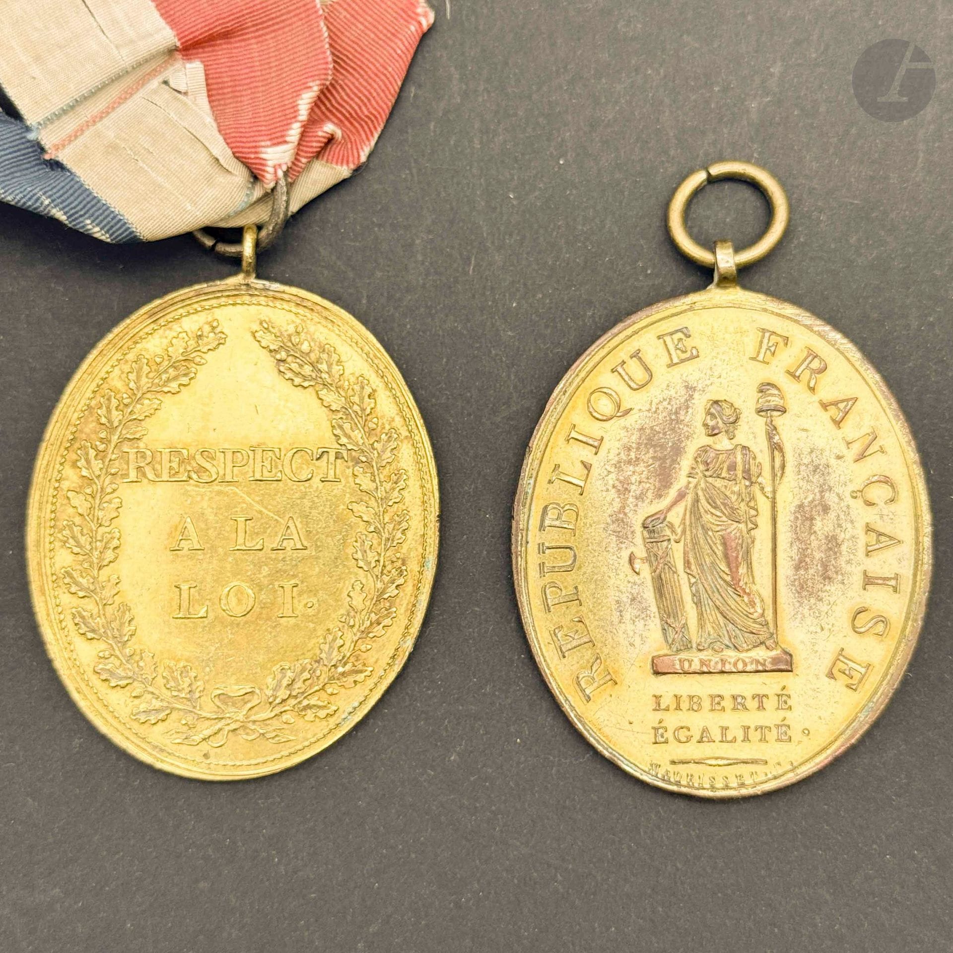 FRANCE
Deux insignes de magistrat ou de fonctionnaire en laiton doré. 
- un signé de Maurisset. Avers à la République française sur socle marqué « union » signé de Maurisset. Revers marqué « respect à la loi ». 
59 x 44 mm
- un marqué « respect à la loi » sur les deux faces, fragments de ruban tricolore en soie et moire. Ancienne collection Professeur Démogé. 
50 x 42 mm
A.B.E. Époque révolutionnaire.
