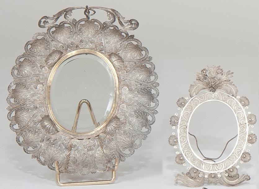 Grand cadre à portrait à suspendre en filigranes d'argent, de forme ovale, le verre biseauté (léger accident) ceinturé d'une bordure en vermeil à rang de filets et de quatre coquilles en filigrane rapportées. Probablement Italie XIXe siècle. Long.: 21,5 cm - larg.: 17 cm Poids brut: 240 g Petits accidents. Cadre à portrait à poser en argent filigrané. Probablement Espagne XXe siècle siècle. Long.: 14,2 cm - larg.: 10 cm Poids brut: 52 g Petits accidents.