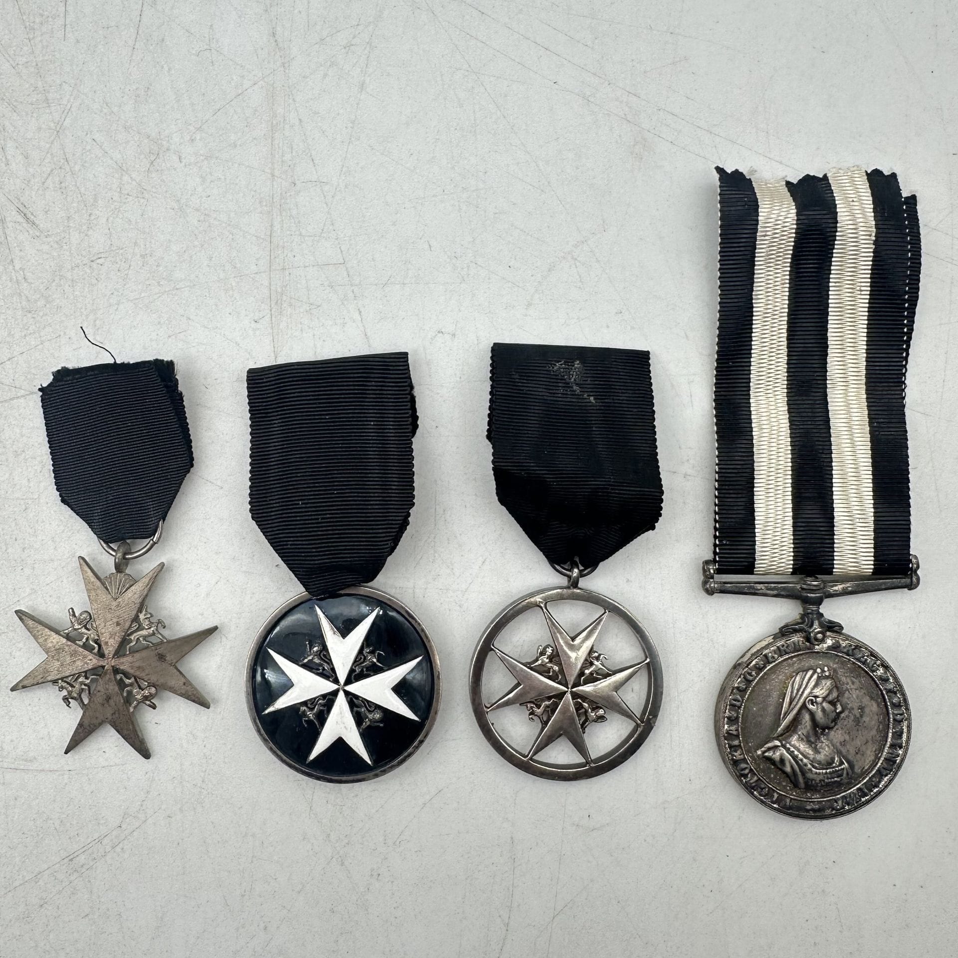 GRANDE-BRETAGNE 
VÉNÉRABLE ORDRE DE L’HÔPITAL DE SAINT-JEAN DE JERUSALEM 
Trois insignes de l’ordre et une médaille : 
- Une de « serving brother », en argent, à fond émaillé noir orné d’une croix émaillée blanche (petits éclats). 38 mm - Poids brut : 32 g 
- Une ronde, ajourée à la croix, en métal argenté. 38 mm 
- Une en métal argenté. Rubans. 39 mm T.T.B. 
- Médaille de service attribuée à « N.Z. 428 S. NEIL », en métal argenté, attribuée sur la tranche. Ruban. 35 mm