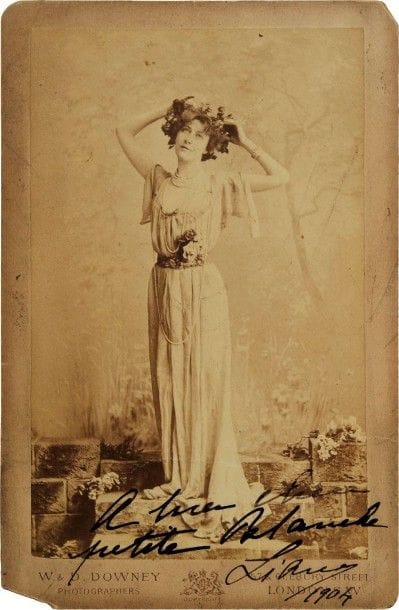 Liane de POUGY (1873-1950) demi-mondaine de la Belle Époque, elle devint Princesse Ghika. Photographie avec dédicace autographe signée « Liane », 1904 ; 14,5 x 9 cm montée sur carte du photographe W. & D. Downey à Londres (16,5 x 11 cm, manque un coin au carton).
Portrait en pied de Liane couronnée de fleurs : « à ma chère petite Blanche Liane 1904 ».
