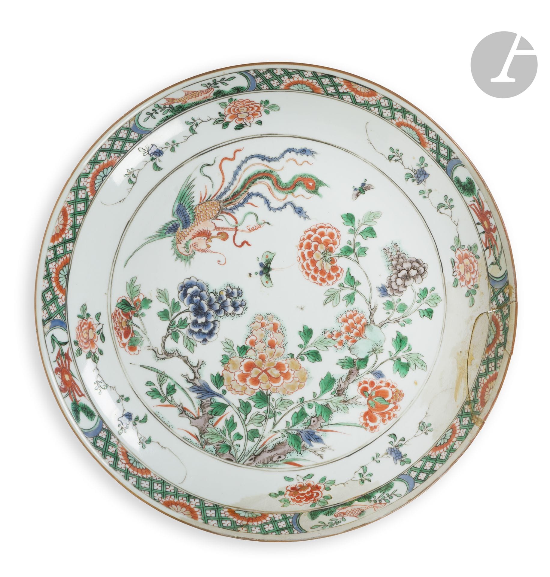 Plat rond en porcelaine de la famille verte à décor de pivoines et fenghuang, Chine, époque Kangxi (1662-1722)
À décor central d’un fenghuang, d’insectes et de deux petits papillons en vol au-dessus de nombreuses pivoines entouré de trois branches des mêmes fleurs. Quatre réserves décorées de crabe et poisson sur un fond à motif géométrique et de demi-chrysanthème stylisés bordent le bord du plat. Au revers du marli quatre branches de pivoines et un double cercle émaillé en bleu sous couverte à la base.
Diamètre : 31,2 cm 
Cassé et recollé, restaurations, sauts d’émail.