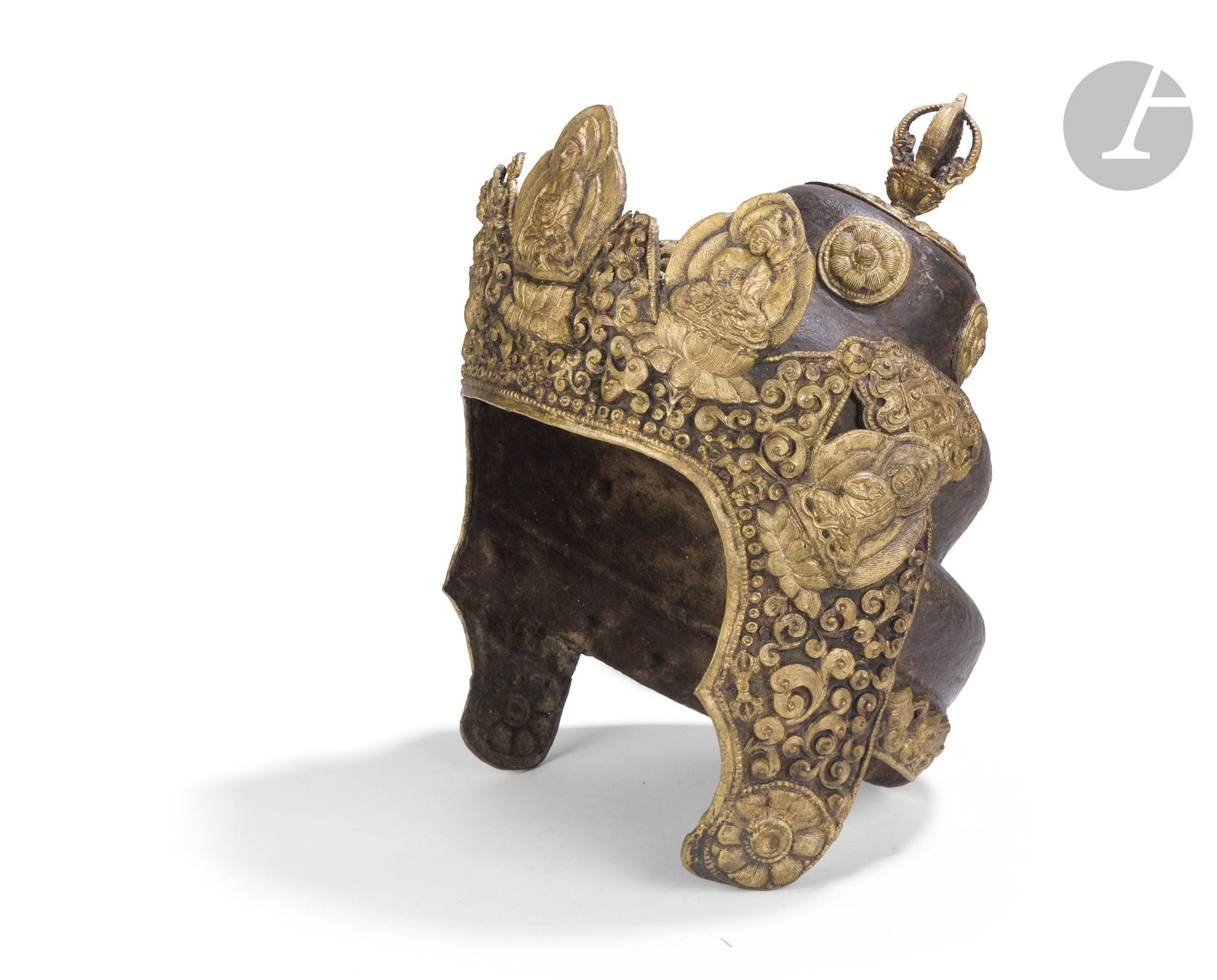 Couronne rituelle de prêtre Vajrācārya Népal ou Tibet, XIXe-XXe siècle 
En alliage de cuivre à patine brune, ornée d’éléments en cuivre doré, repoussé et ciselé. Le dôme à deux registres repose sur une base circulaire évasée et est sommé d’un vajra à cinq branches ajourées. Le décor associe rosaces, rinceaux végétaux, motifs perlés et symboles bouddhiques, notamment le nœud sans fin śrīvatsa. La bordure de la base est ornée de médaillons lotiformes figurant les cinq bouddhas cosmiques, Vairochana, Akshobhya, Ratnasambhava, Amitabha et Amoghasiddhi, représentés assis en méditation. Les côtés retombants sont décorés de motifs végétaux et de rangs de perles. L’ensemble présente une patine sombre, des usures de dorure, quelques déformations et lacunes, ainsi que des traces d’oxydation et de corrosion.
Hauteur : 30,5 cm