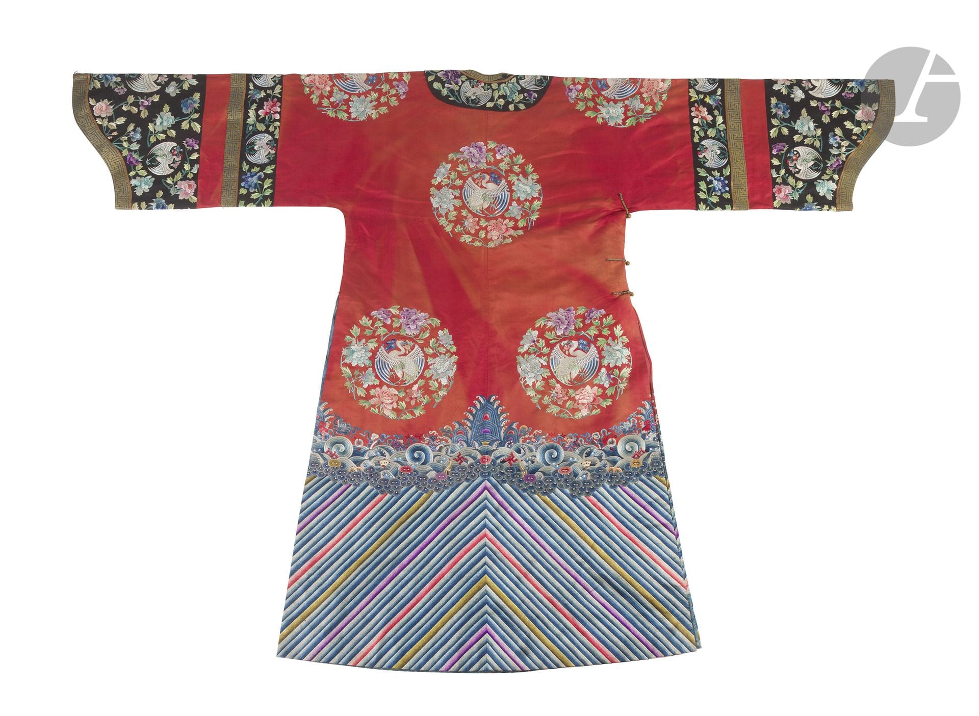 Robe de cour informelle de femme en soie à fond rouge, Chine, fin du XIXe siècle
La robe à larges manches « sabot » de style mandchou, fendue sur les côtés, ferme sur le côté droit par cinq boutons en alliage de cuivre. Le bas montre les classiques vagues de l’Océan d’où émergent les rochers de la Terre flanqués de deux dragons et d’objets de bon auspice au-dessus d’une haute bande lishui. Le devant, le dos et les épaules sont brodés en fils de soie polychromes de huit médaillons formés chacun par une grue aux ailes déployées entourée de fleurs de pivoines. Le bord du col et les manches, en soie noire, reprennent le même motif de grues et pivoines et sont bordés d’une soie en fil d’or et bleu à décor géométrique.
Longueur : 141 cm ; largeur : 204 cm
Quelques taches, usures et décoloration.

Une robe très similaire est conservée au Minneapolis Institute of Arts et reproduite dans Imperial Silks - Ch’ing Dynasty Textiles in The Minneapolis Institute of Arts, N°103-104 cc. no. 42.8.64