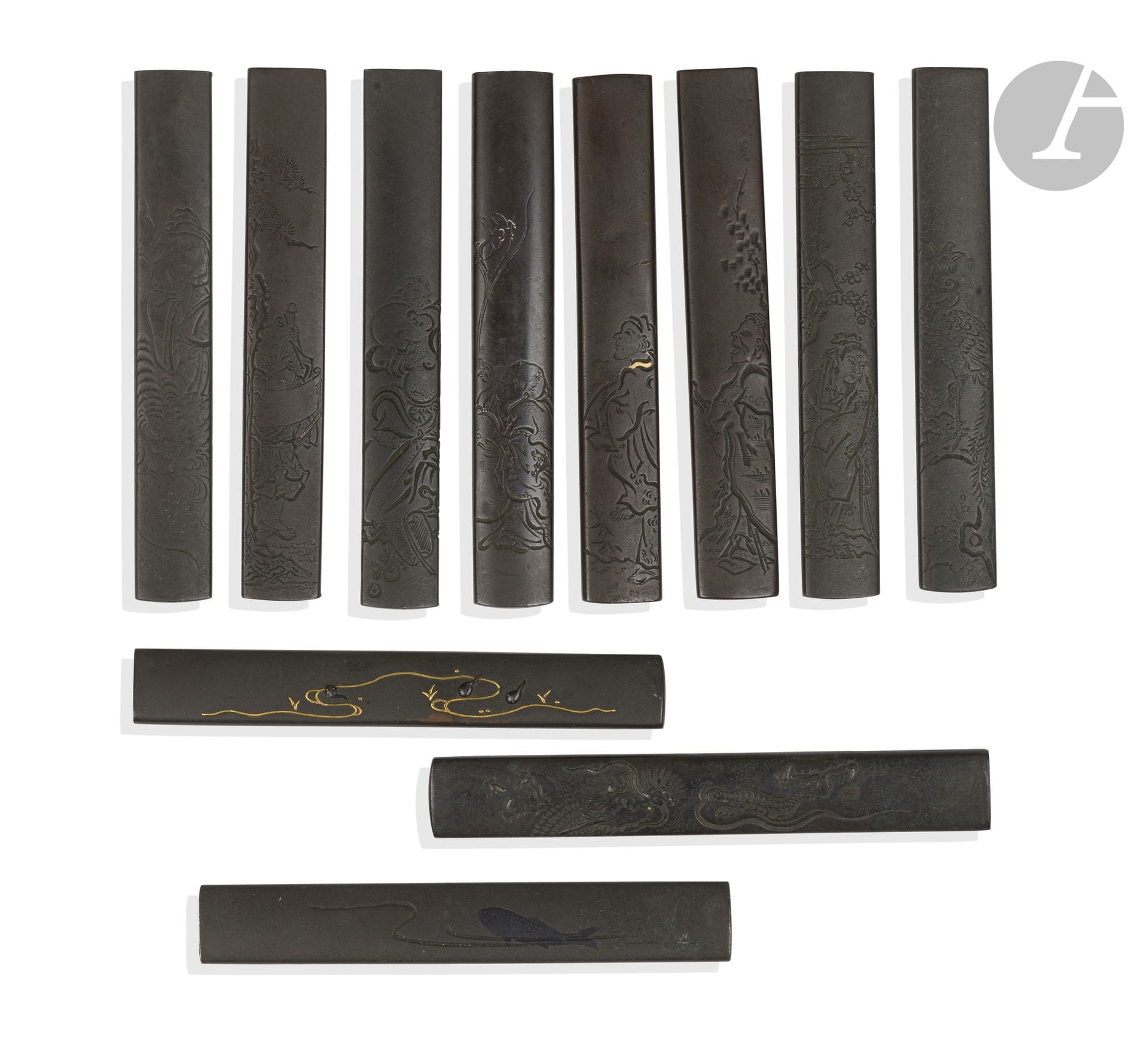 Onze kozuka en shibuichi et fer, Japon, époque Edo (1603-1868)
- Un en shibuichi non signé à décor en katakiri bori d’un phénix (plaque arrière en partie désoudée). - Un en shibuichi incrusté en takazogan or et shakudo de têtards dans l’eau. Il est signé au dos Hosono Sōzaemon Masamori - 細野惣左衛門政. - Un en shibuichi à décor en katakiri bori du sennin Chokwaro. Signé au dos Tsunekatsu saku - 序克作. - Un en shibuichi à décor en katakiri bori d’un tigre regardant son reflet dans l’eau, accompagné d’un dignitaire chinois. Signé au dos Kwaryudō Bokusen - 花竜洞　牧川 avec kao. - Un en shibuichi à décor en katakiri bori d’un dignitaire chinois sous un prunier en fleurs. Porte à l’arrière une signature Somin - 宗珉 avec kao sur une plaque en shakudo. - Un en shibuichi à décor en katakiri bori d’un yamabushi lisant un makimono sous un pin. Porte à l’arrière une signature Somin - 宗珉. - Un en shibuichi à décor en katakiri bori et takazogan d’un dragon dans des nuées. Signé à l’arrière Hakuryusai - 白龍斉. Fendu sur le côté. - Un en shibuichi à décor en katakiri bori et hirazogan d’un personnage chinois tenant dans ses mains un rat. Signé à l’arrière Yanagawa Naomasa - 栁川直政. - Un en shibuichi à décor en katakiri bori de Hotei, son éventail et le tama à ses pieds. Signé au revers Hidetoshi - 英利 avec kao. - Un en shibuichi à décor en katakiri bori d’un sennin sous un arbre. Signé au revers Tomotake - 友武. - Un en shibuichi à décor en katakiri bori et hira zogan d’une carpe sortant de l’eau. Signé au revers de manière difficilement lisible, probablement Ichijō 一乗 suivi d’un kao.