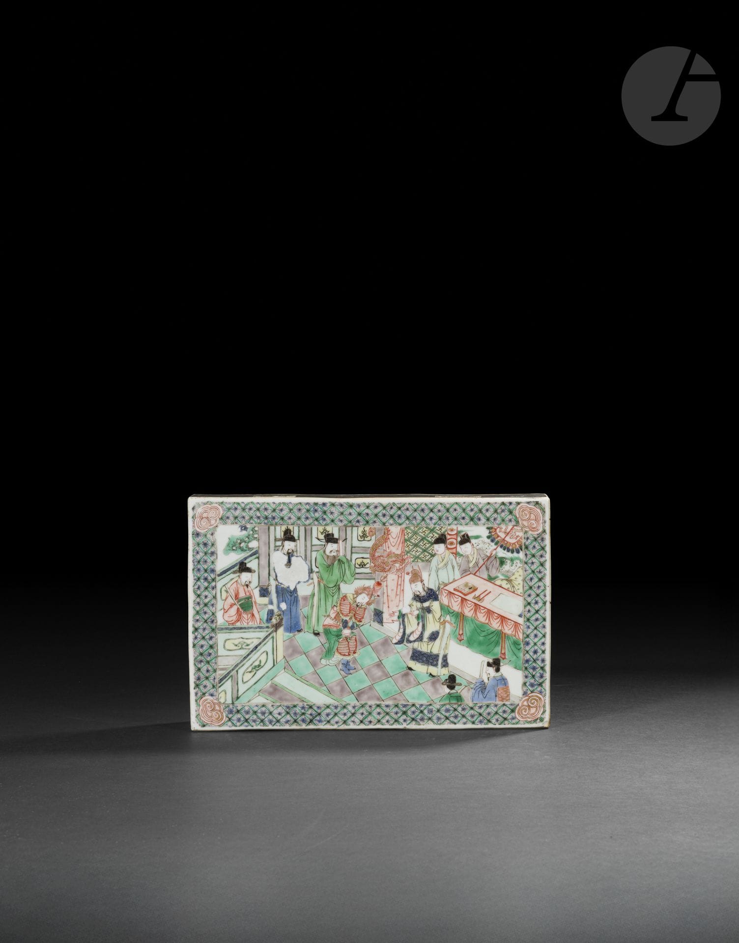 Brique en porcelaine de la famille verte, Chine, époque Kangxi (1662-1722)
De forme rectangulaire, cette plaque en porcelaine est décorée sur ses deux faces de scènes peintes en émaux polychromes dans le style de la famille verte. L’une présente, au centre d’une large bordure ornée de motifs floraux et feuillagés sur fond vert, un paysage montagneux animé d’un vaste plan d’eau, de pavillons, muraille et pagodes dans la végétation, de rochers et d’arbres en fleurs ; une petite embarcation est représentée sur le lac, tandis qu’un poème peint à l’or dans la partie supérieure gauche, accompagné de sceaux rouges, complète la composition. L’autre face est consacrée à une scène historique et morale inspirée de l’épisode célèbre de Fù jīng qǐng zuì - 负荆请罪, littéralement « porter les branches épineuses pour demander pardon », tiré de l’histoire du général Lian Po et du ministre Lin Xiangru. La scène se déroule dans un intérieur palatial : plusieurs dignitaires vêtus de longues robes sont réunis autour du roi de Zhao, tandis que Lian Po, reconnaissable à son attitude humble, vient présenter ses excuses à Lin Xiangru. Les personnages sont disposés devant un mobilier de cour et parmi des éléments architecturaux richement décorés, notamment des tables, sièges et motifs de dragons ; l’ensemble est encadré d’une large bordure géométrique et de motifs stylisés de nuages ou de rinceaux aux angles. La représentation illustre le moment où le général, ayant reconnu la grandeur d’esprit de Lin Xiangru qui avait volontairement évité l’affrontement avec lui, vient faire amende honorable. La légende constitue une illustration du principe confucéen selon lequel l’ambition, le prestige et la fierté doivent être tempérés par la modestie et la capacité à reconnaître ses torts ; elle souligne également que les intérêts de l’État et l’harmonie entre ses serviteurs doivent primer sur les rivalités et querelles personnelles. 
26 x 17 x 4,5 cm
Manques d’émail bleu et usures dans la dorure.