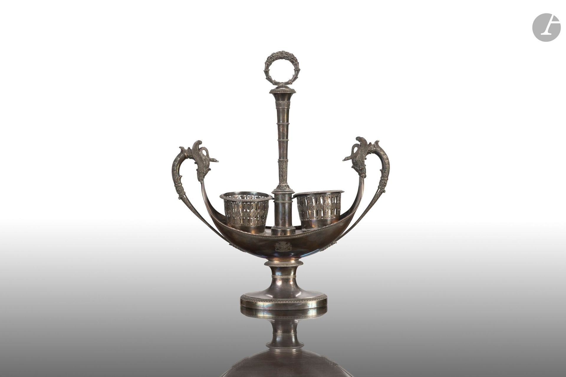 950°/°° silver carafe designed to hold an oil and vinegar set, featuring handles decorated with swans with outstretched wings and a central banded body; the handle is shaped like a laurel wreath, and the body is engraved with the coat of arms of the Marquises of Arcangues. 
Paris, 1809–1819. 
H.: 40 cm - W.: 33 cm
Net weight: 1234 g

This lot comes from the reception hall of the Château d’Arcangues.