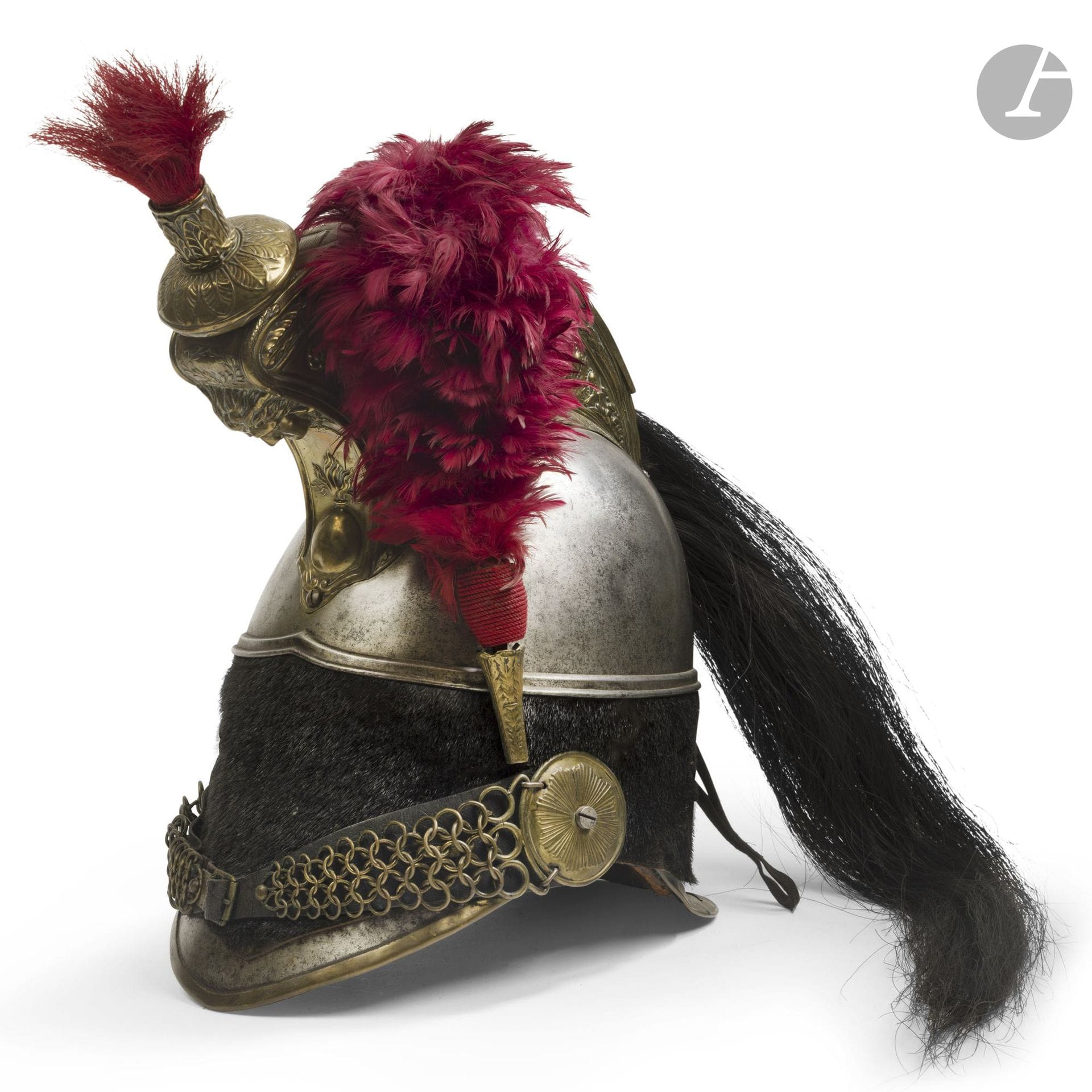 1845-model cuirassier helmet for the infantry.
Steel helmet shell marked “137,” “45,” “6,” and stamped “LR.” Crest featuring a jellyfish head surmounting a flaming grenade on the front, with fluted sides, a rim, leather-lined chain chinstraps, rosettes with a radiating background, and a plume holder and marmot made of stamped brass. Turban made of navy blue cowhide with lacing at the back. Black horsehair mane and red horsehair plume on the marmot. Leather inner lining (minor imperfections) and scarlet plume.
A.B.E. (One crest screw replaced; period crest reattached).
