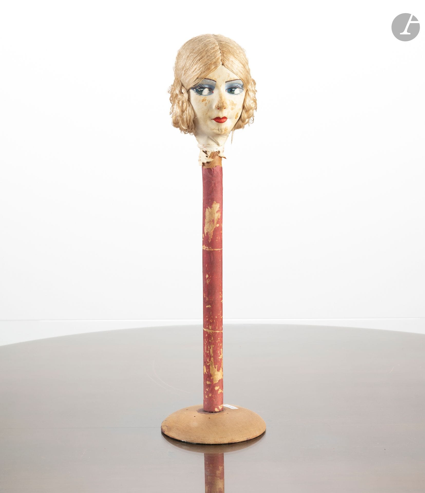 Porte chapeau en bois sommé d'une tête de poupée à la perruque blonde. 
Début du XXe siècle. 
H. : 48 cm
(Usures, lot vendu en l'état).