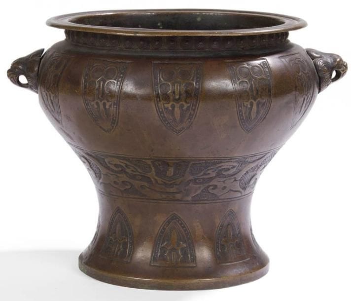 JAPON - Vers 1900
Vase à panse haute en bronze à patine brune à décor incisé de masques de taotie et frises de cigales stylisées. Deux anses en forme de têtes de chimères. H.: 16 cm Manque les anneaux