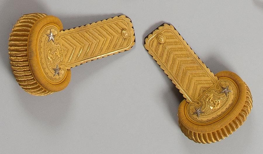 Paire d'épaulettes de contre-amiral. Corps brodé de canetille et paillette or, à deux étoiles en argent et motif à l'ancre encablée en bronze doré, ciselé. Grosses torsades or. Boutons dorés au règlement des officiers généraux de la Marine. Doublure de velours bleu nuit. Attaches marquées du fabricant Gautier Fils à Toulon Dans sa boîte en carton avec étiquette du fabricant. T.B.E. État neuf. IIIe République.
