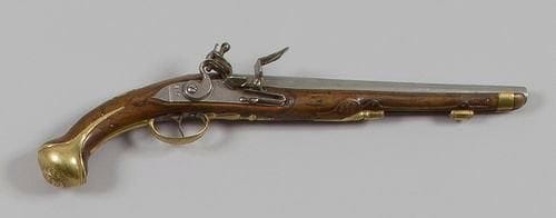 Pistolet d'officier à silex type 1733/1734. Canon rond à pans au tonnerre, gravé de feuillages au tonnerre. Point de mire en laiton. Platine et chien col de cygne décoré au trait à corps plat. Bassinet à pans, en fer. Garnitures en laiton, découpé et gravé de frises. Calotte à longue oreille en laiton, clou de calotte ciselé d'un masque grimaçant. Crosse en noyer sculpté (petite restauration au niveau de la calotte). Pièce de pouce en laiton découpé, gravée d'une fleur de lys et «RMH» (?) L. canon: 31 cm - L. totale: 49 cm A.B.E. (Manque la baguette).