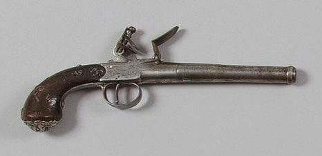 Pistolet à coffre à silex anglais dit «Queen Ann». Long canon rond à bourrelet à la bouche, à balle forcée. Coffre avec restes de gravure «BUNNEY» «LONDON» dans des banderoles. Chien et pontet en fer décoré au trait. Crosse en noyer incrusté de fil d'argent (manques) à décor feuillagé. Pièce de pouce en argent gravé d'armoiries aux trois têtes de mort sous couronne de marquis. Calotte en argent poinçonné ornée d'un masque grimaçant (vis postérieure). A.B.E. Vers 1800. BUNNEY à Birmingham et Londres vers 1780-1800