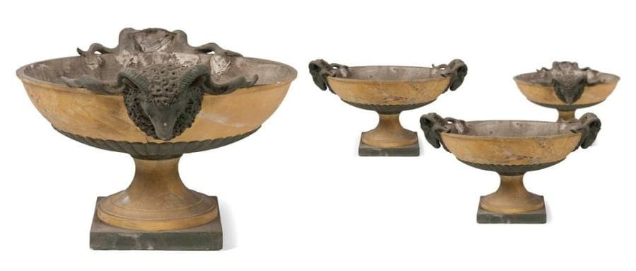 Suite de quatre grandes coupes d'ornement en tôle peinte en faux marbre jaune et faux bronze à patine vert antique, à décor de têtes de bélier; reposant sur des piédouches en plâtre peint. Milieu du XIXe siècle. Accidents et restaurations. H.: 38 cm - L.: 64 cm - P.: 52 cm