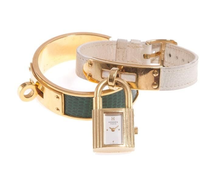HERMES
Montre de dame en métal doré, modèle Kelly, fond blanc, index pointé, bracelet en cuir blanc à boucle ardillon. Numérotée. Dans son écrin. Accompagnée d'un bracelet en lézard vert monté en métal doré