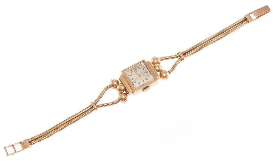 Montre de dame en or jaune, cadran carré, fond satiné, index chiffres arabes, les anses en boules d'or, bracelet double chaînette serpent. Travail français vers 1945. Poids brut: 27,5 g (remontoir métal, mouvement à réviser)
