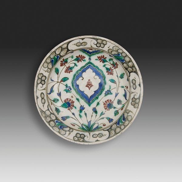 Plat tabak à la mandorle, Turquie ottomane, Iznik, XVIIe siècle Céramique siliceuse à base annulaire à décor peint en polychromie sous glaçure transparente sur fond blanc. Décor de mandorle en réserve sur fond bleu bordée de fleurs. Au rebord, frise de vagues et rochers noirs à rehauts bleus et verts. Alternance de volutes en spirales bleues et vertes au revers. État: fracturé en cinq parties. Diam.: 30 cm; H.: 3,8 cm Provenance: ancienne collection Brimo de Larrousilhe.


An Iznik pottery dish, Tabak, decorated with a central ogival medallion, Ottoman, Turkey, 17th century