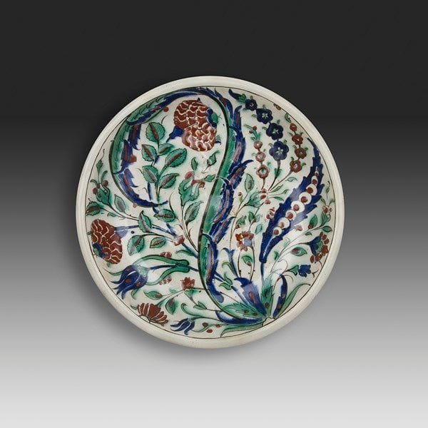 Plat au bouquet, Turquie ottomane, Iznik, début du XVIIe siècle Grand plat en céramique à pâte siliceuse à décor peint en polychromie sur fond blanc, sous glaçure transparente. Une palme à double courbure bicolore, flanquée d?une plus petite garnie d?églantines stylisées sur fond bleu, s?épanouit sur un bouquet d?églantines et de gros oeillets. Diam.: 32 cm État: bord tronqué et restauré. Provenance: Ancienne collection Brimo de Laroussilhe.
 

An Iznik polychrome pottery dish, decorated with a central whirling palm leaf, Ottoman Turkey, 17th century