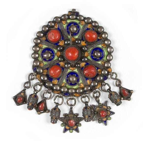 Grande fibule ronde, Algérie, Tabzmit, Grande Kabylie, Benni Yenni, fin du XIXe - début du XXe siècle Argent ciselé, décoré d?émaux cloisonnés jaune, vert et bleu, serti de quatre gros cabochons de corail et d?un autre au centre sur l?épingle de la fibule. Le dos orné d?une rosace stylisée. L?ensemble est agrémenté de neuf pampilles serties de corail. Haut.: 18,5 cm (avec pampilles) - Diam.: 12,5 cm (env.) P: 448 g 


A large round enamelled silver fibulae, Algeria, Great Kabilya, Benni Yenni, late 19th - early 20th century